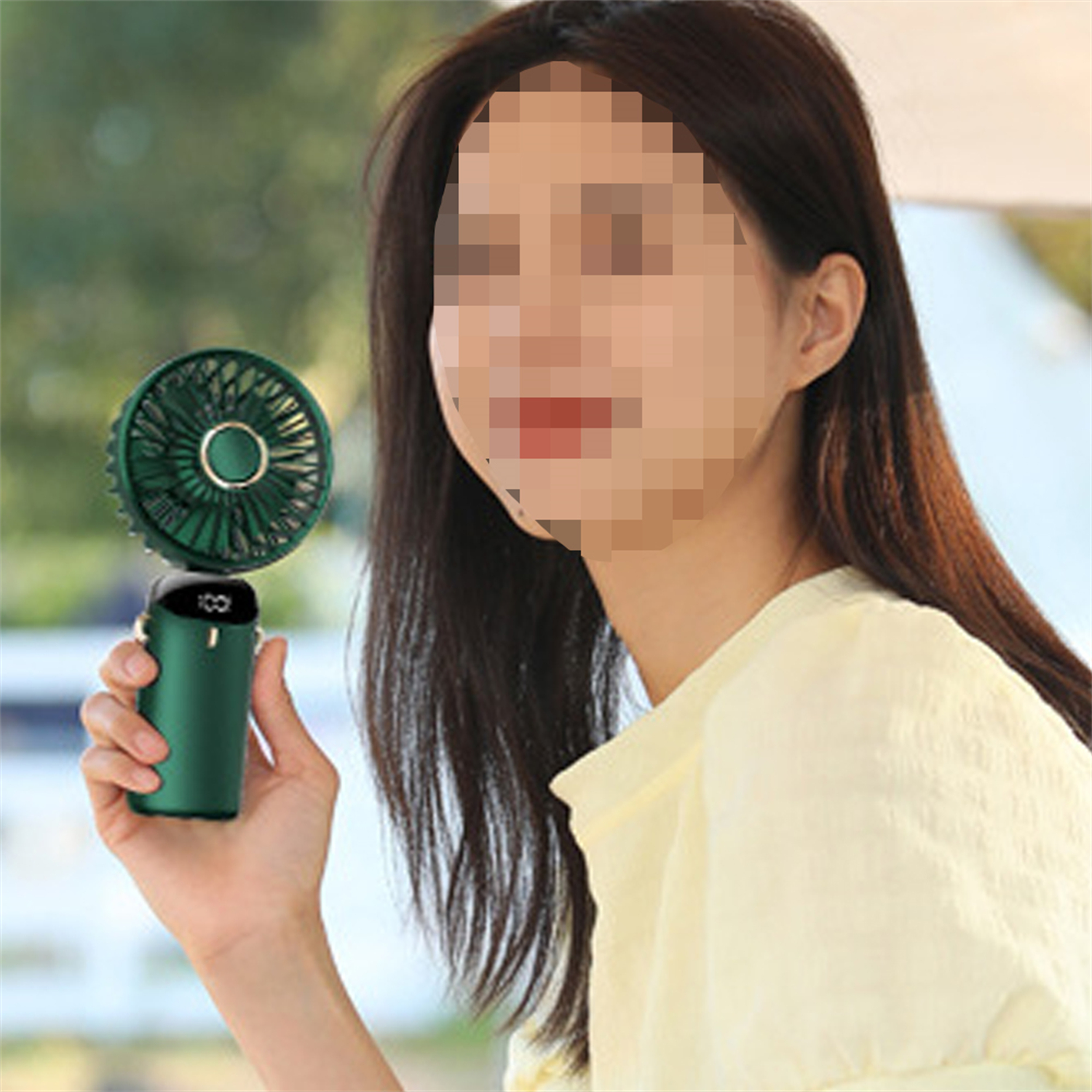 Eine Frau hält einen grünen tragbaren Ventilator. Der Ventilator hat eine Digitalanzeige.