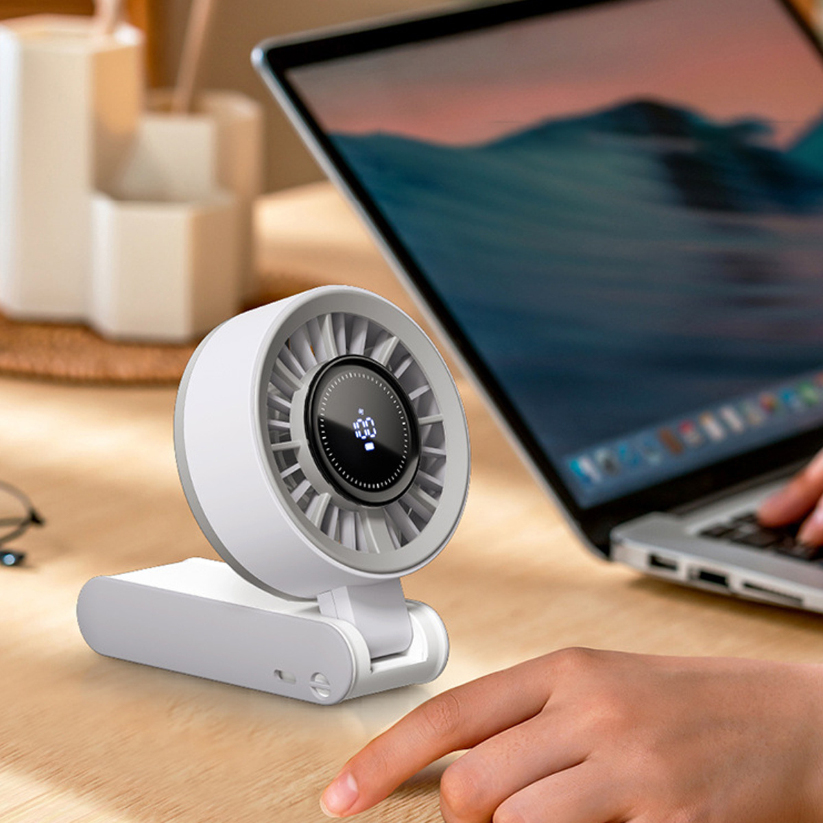 Ein weißer Ventilator auf einem Schreibtisch, angeschlossen an einen Laptop. Ein Finger berührt den Ventilator. Der Ventilator hat eine Anzeige '100'.