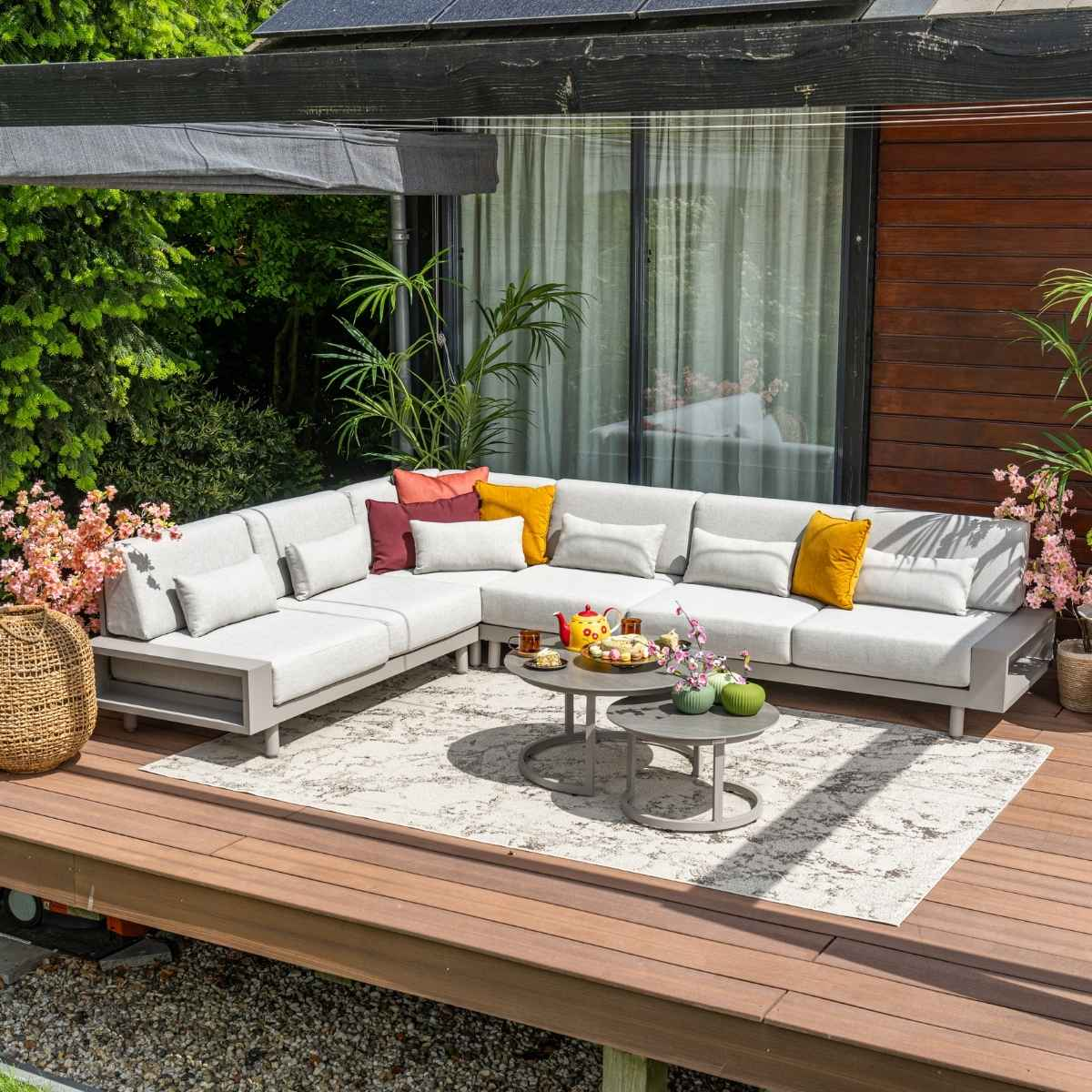 Outdoor scene with L-shaped gray sofa, tables, tea set, and flowers.