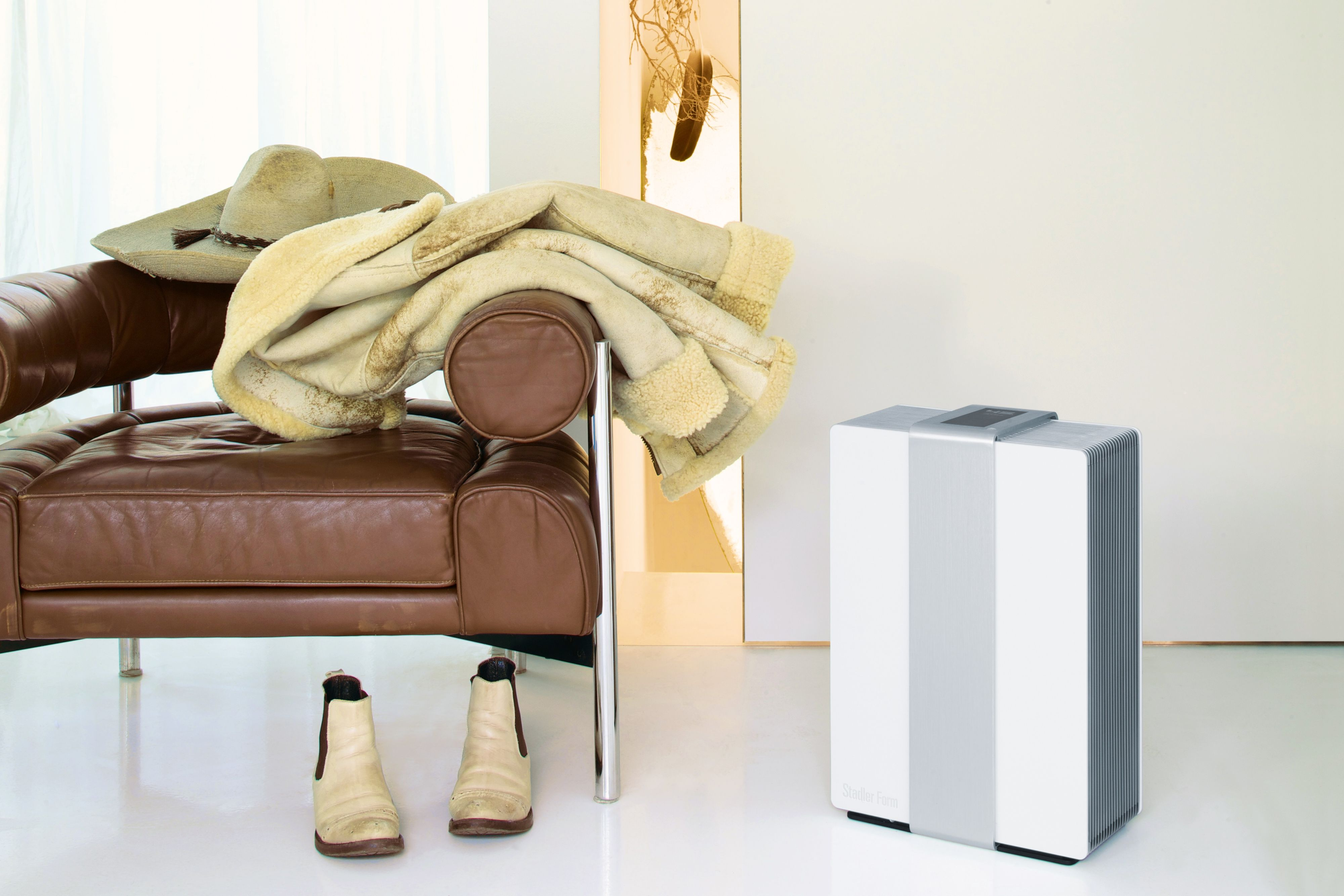 White and silver air purifier, brown leather couch, hat, coat, boots.