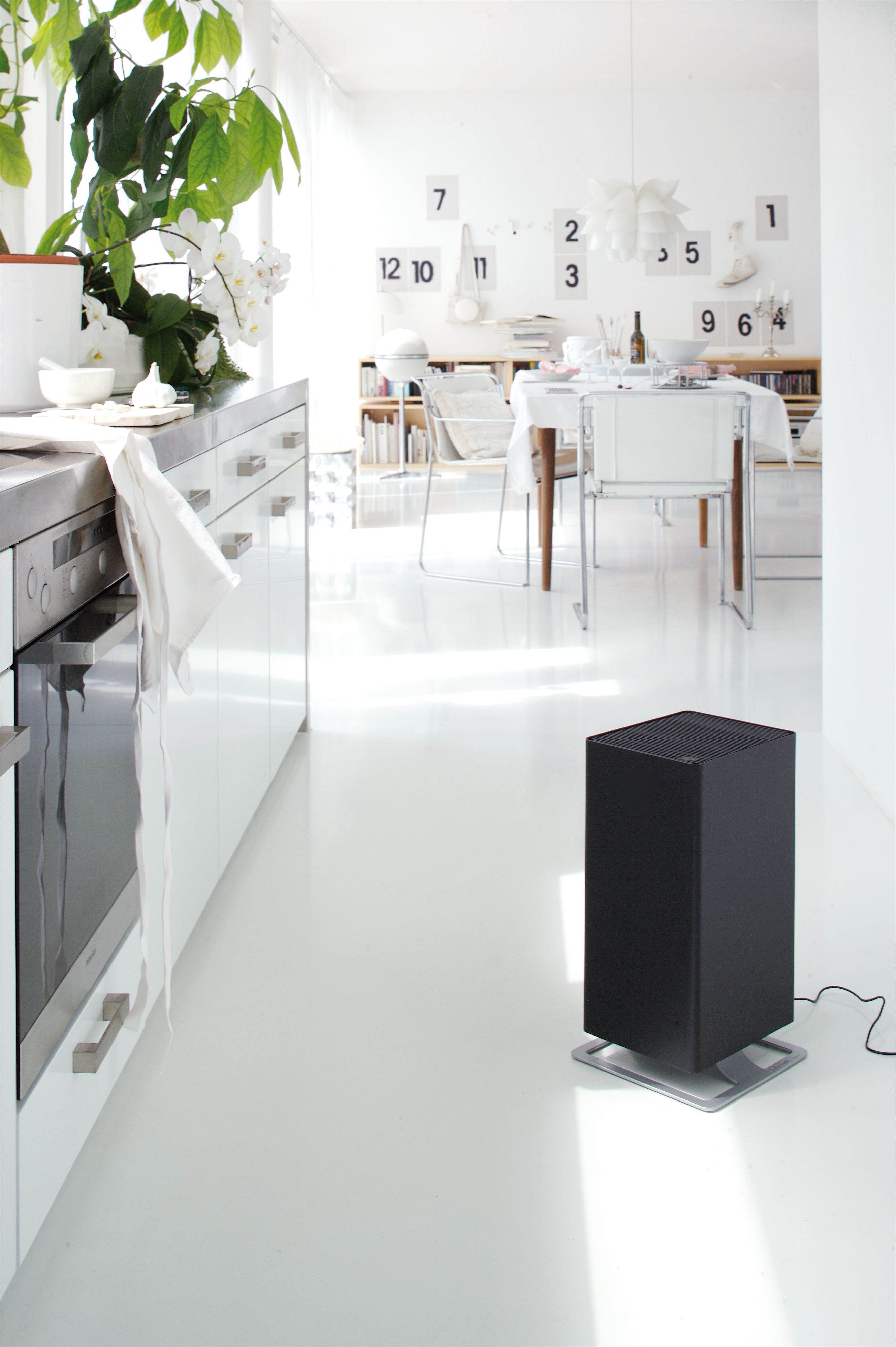 Moderna cucina bianca con purificatore d'aria sul pavimento e zona pranzo sullo sfondo.