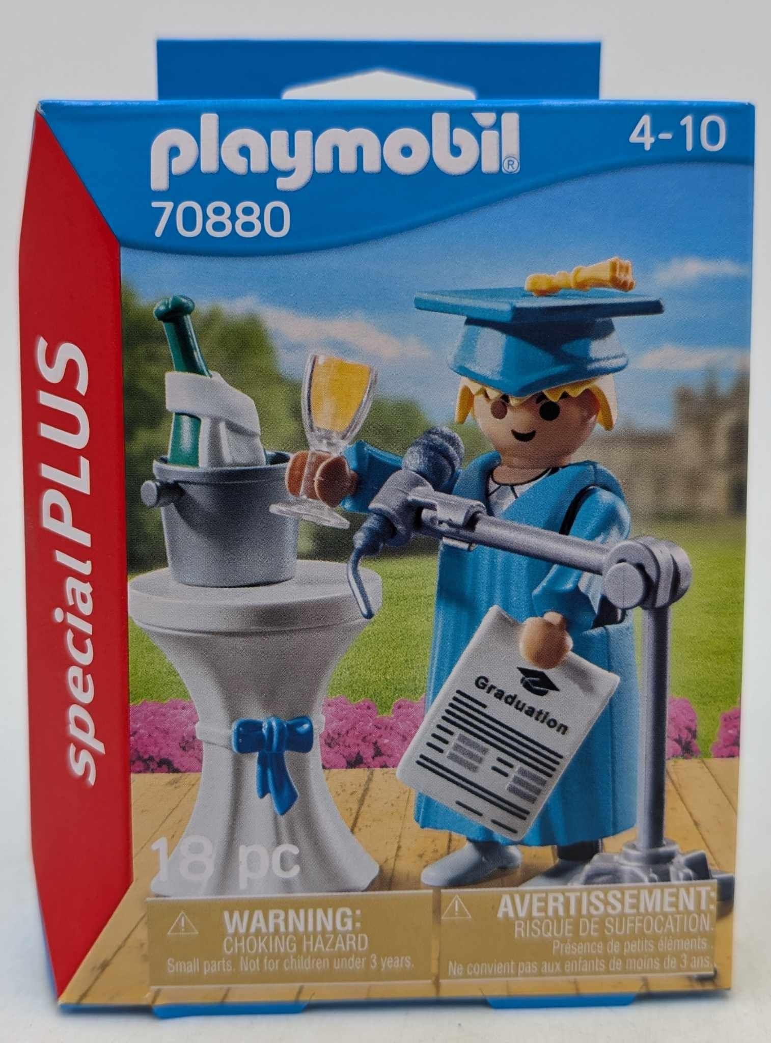 Pudełko Playmobil przedstawia scenę ukończenia szkoły. Postać w niebieskiej szacie trzyma dyplom i kieliszek. Na stole stoi butelka szampana.