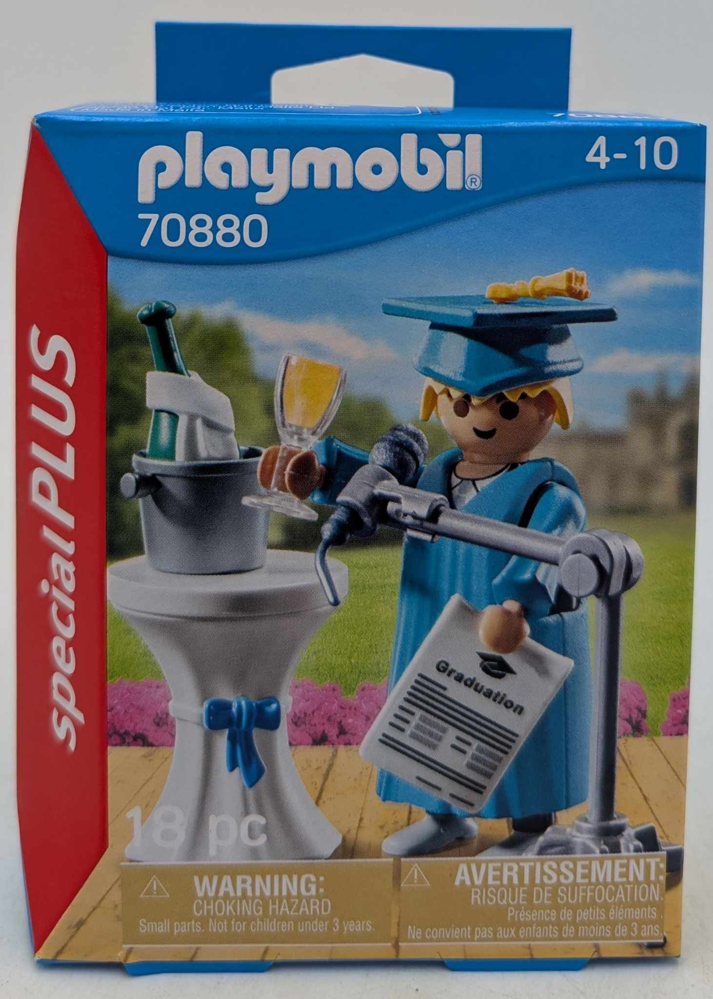 Zestaw Playmobil z okazji ukończenia szkoły. Postać w szacie trzyma mikrofon, dyplom i kieliszek. Na stole szampan i kieliszek.