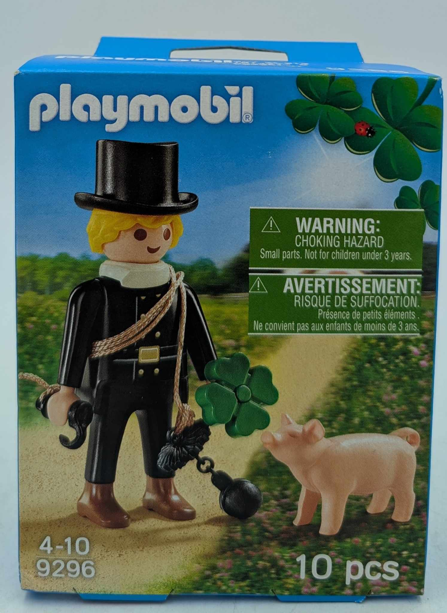 Playmobil-Box: Schornsteinfegerfigur mit Schwein und Klee. Warnhinweis. Grüner Hintergrund.