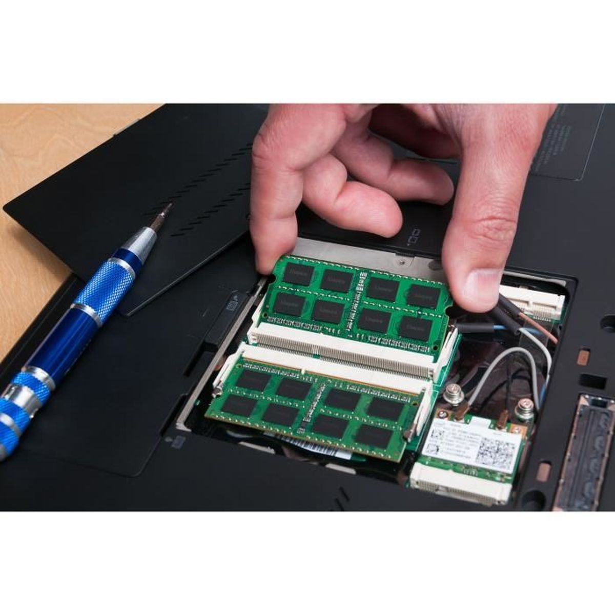 Een persoon installeert RAM in een laptop. Een schroevendraaier en RAM-modules liggen op de tafel.