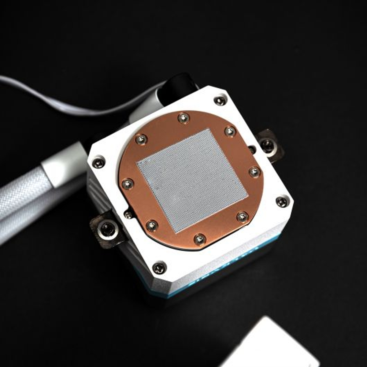 Primer plano de un enfriador líquido de CPU con placa de cobre y marco plateado. Fondo negro.