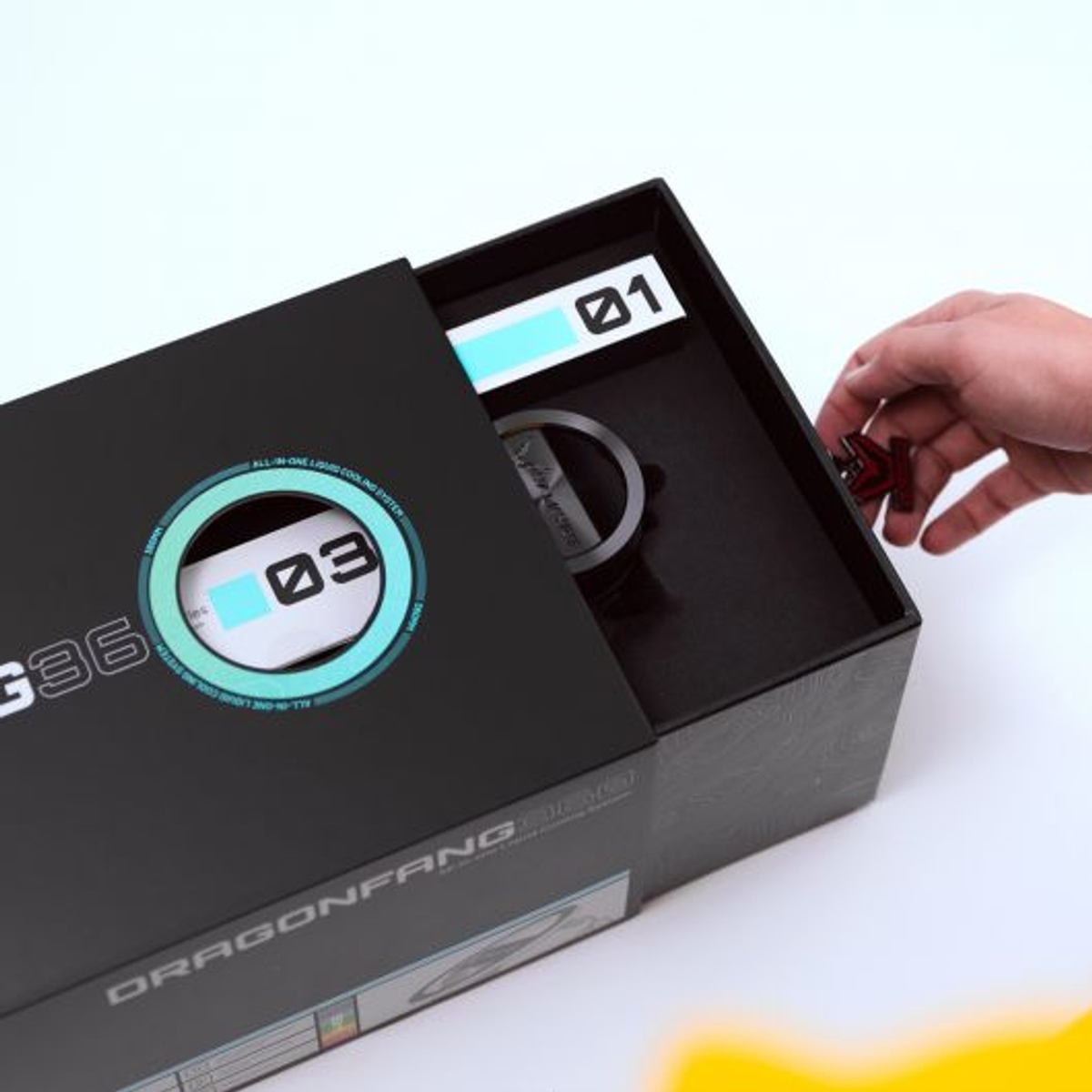 Caja de enfriador de computadora abierta con una mano que alcanza una pieza pequeña. Negro con detalles turquesa.