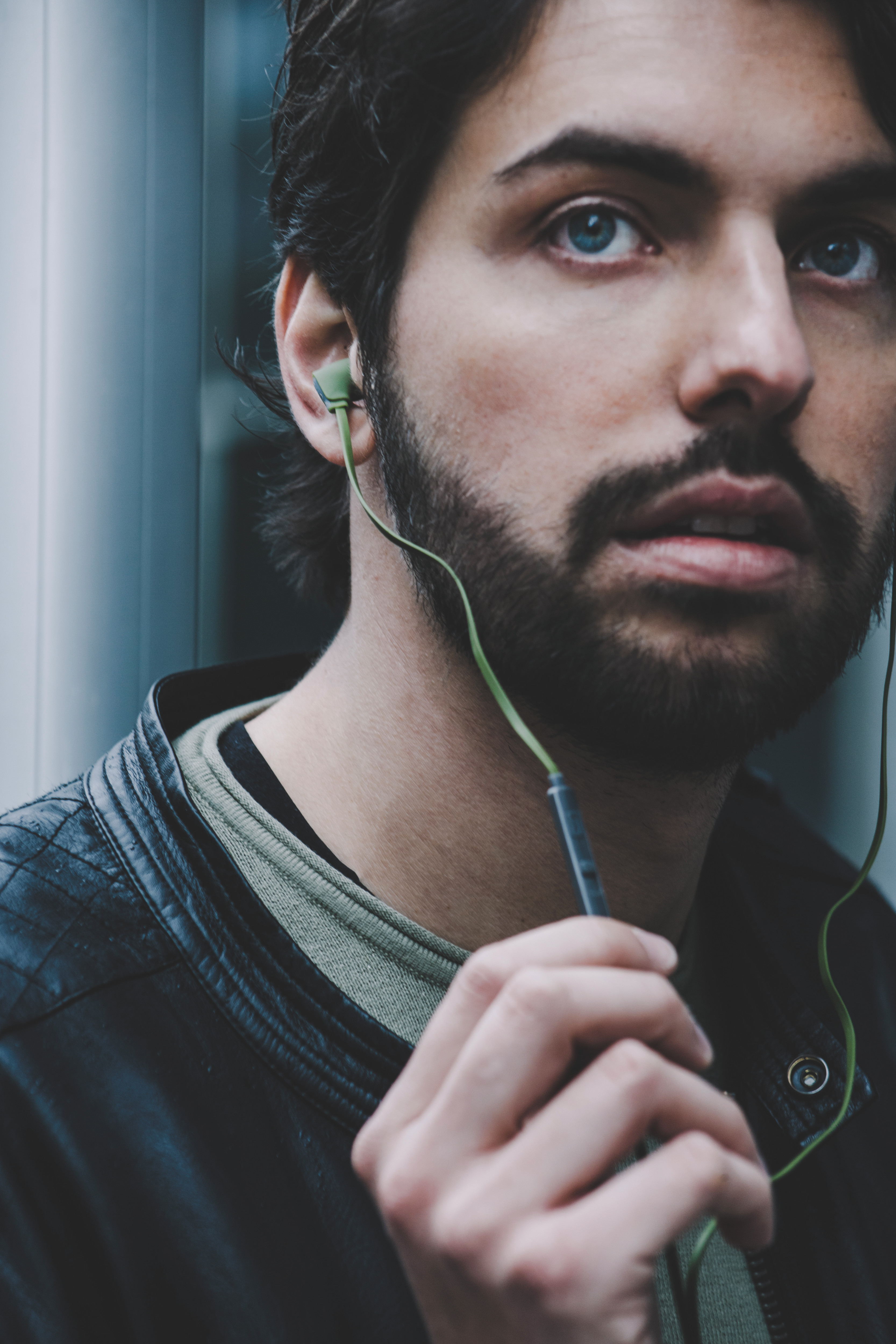 Un uomo con la barba indossa un auricolare verde. Sta tenendo un telefono e guarda leggermente in basso.