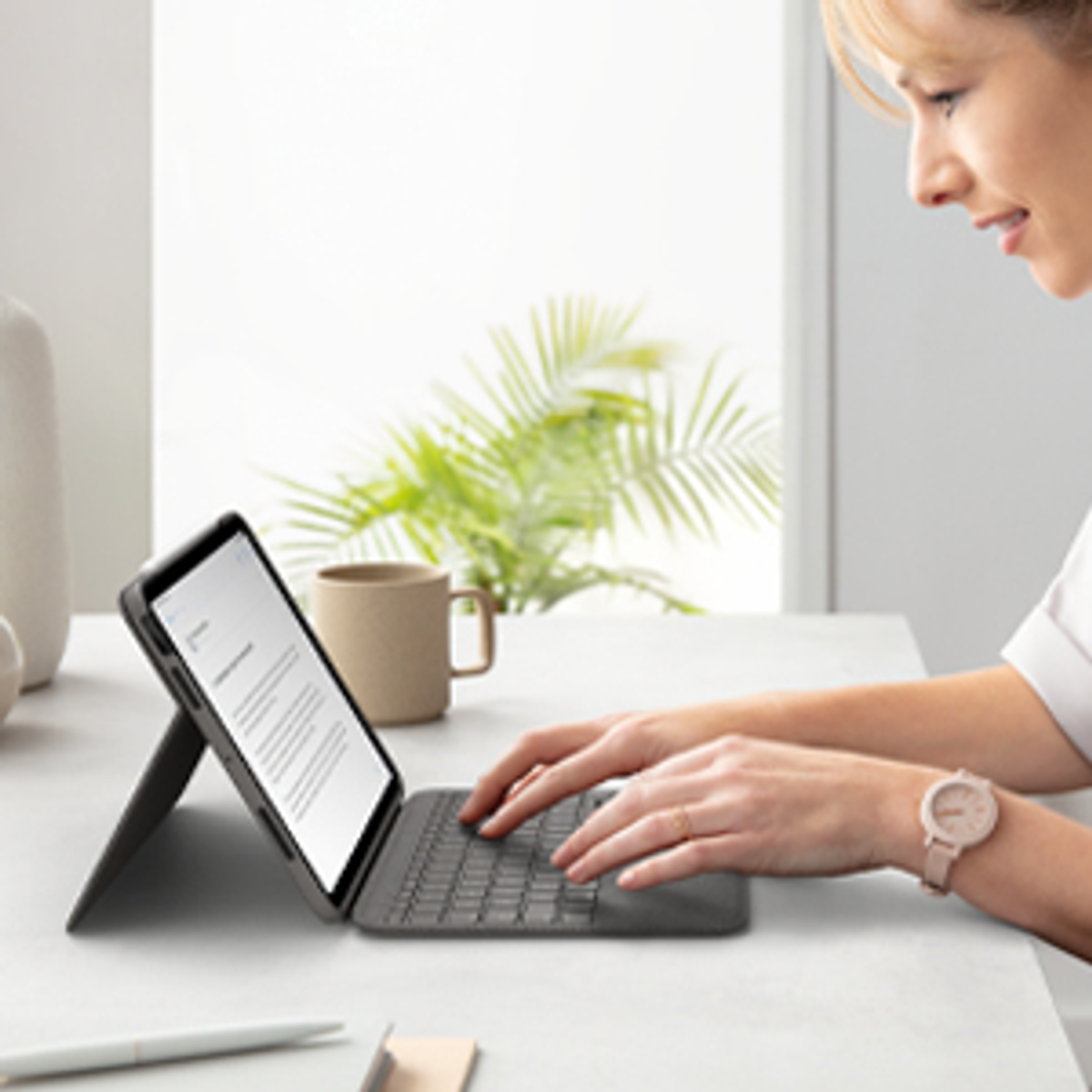Donna che lavora su un tablet con tastiera, in una stanza luminosa.
