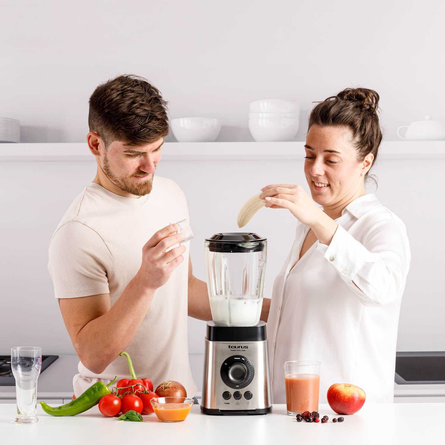 Una pareja agregando un plátano a una licuadora con leche, en un entorno de cocina.