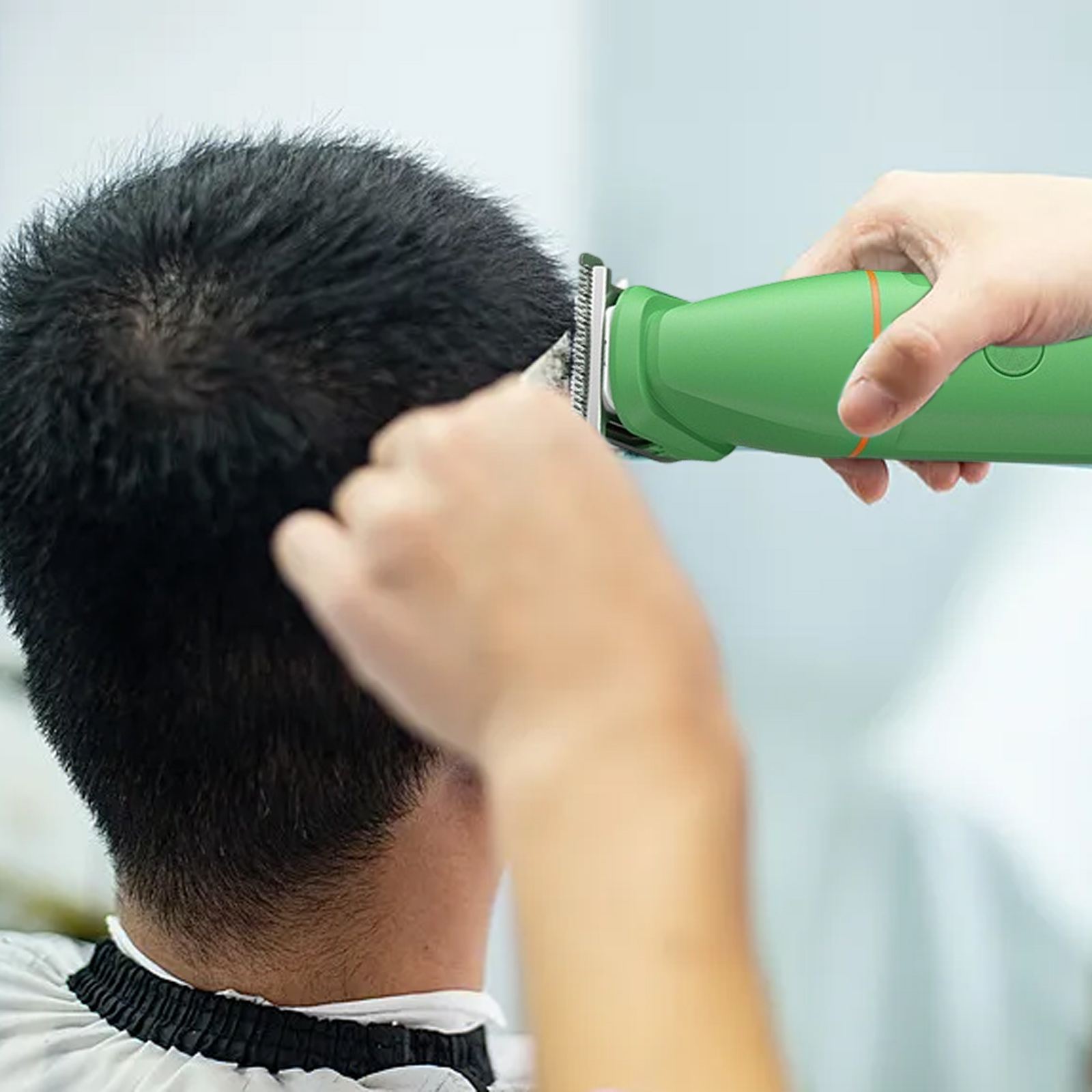 Eine Person schneidet Haare mit einem grünen Trimmer. Der Rücken der Person ist zur Kamera gerichtet. Die Hand einer anderen Person ist sichtbar.