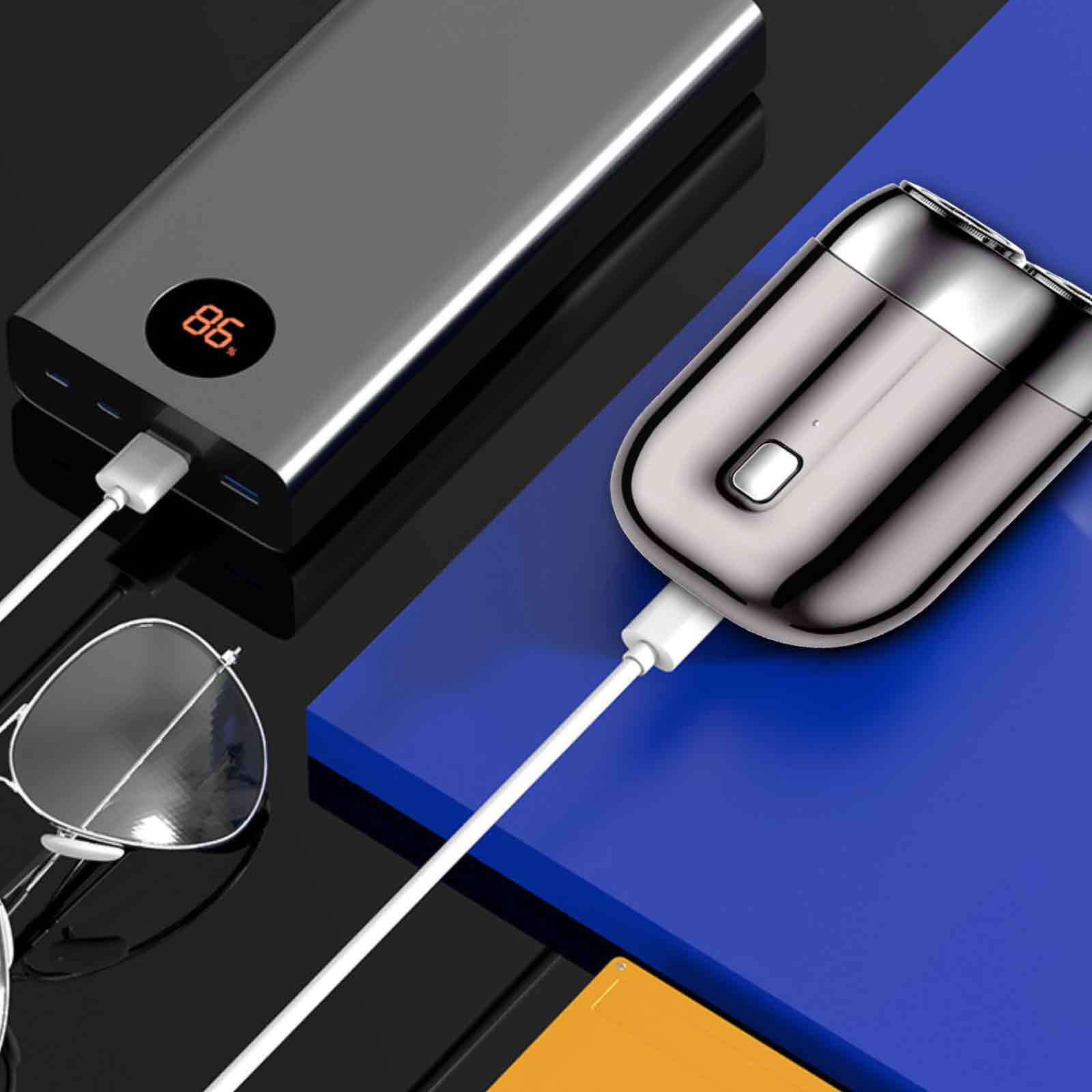 Ein Rasierer wird an einer Powerbank aufgeladen. Brille und blaue Oberfläche sind ebenfalls vorhanden.