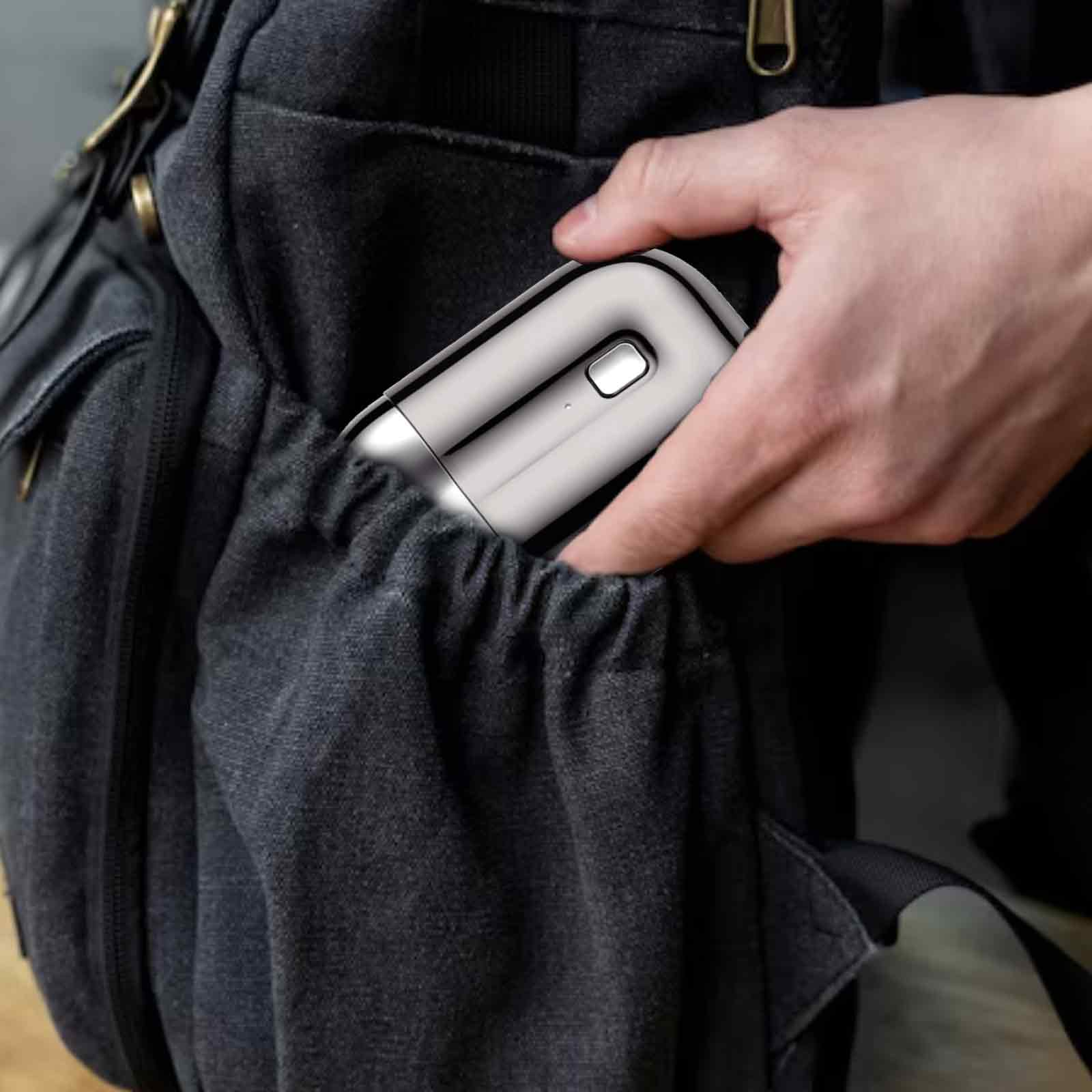 Hand, die einen silbernen Rasierer in eine dunkelgraue Rucksacktasche legt.