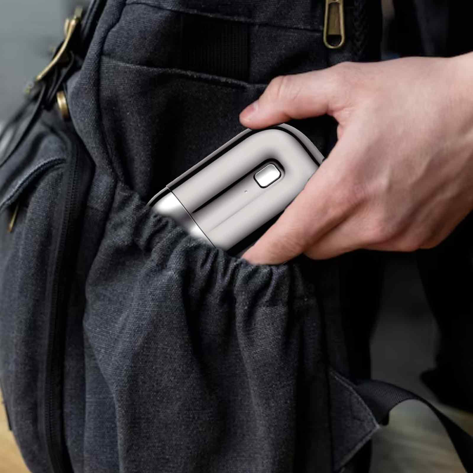 Hand, die einen silbernen Rasierer in eine dunkelgraue Rucksacktasche legt.