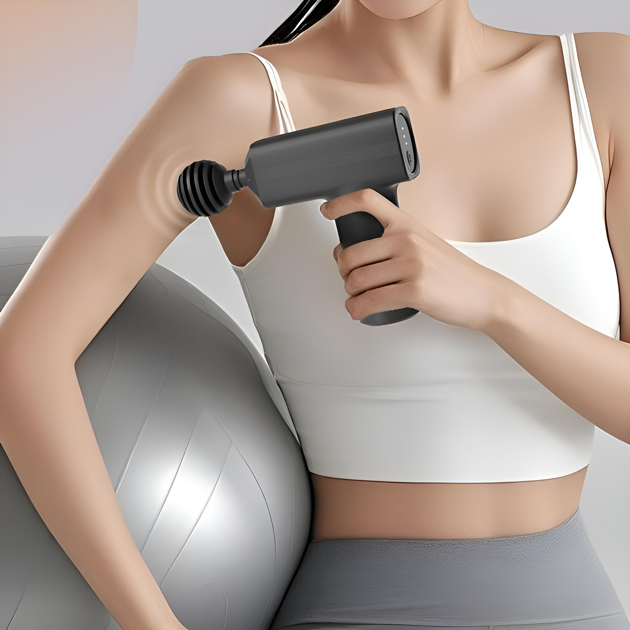 Frau benutzt eine schwarze Massagepistole an ihrem Arm, mit einem grauen Gymnastikball daneben.