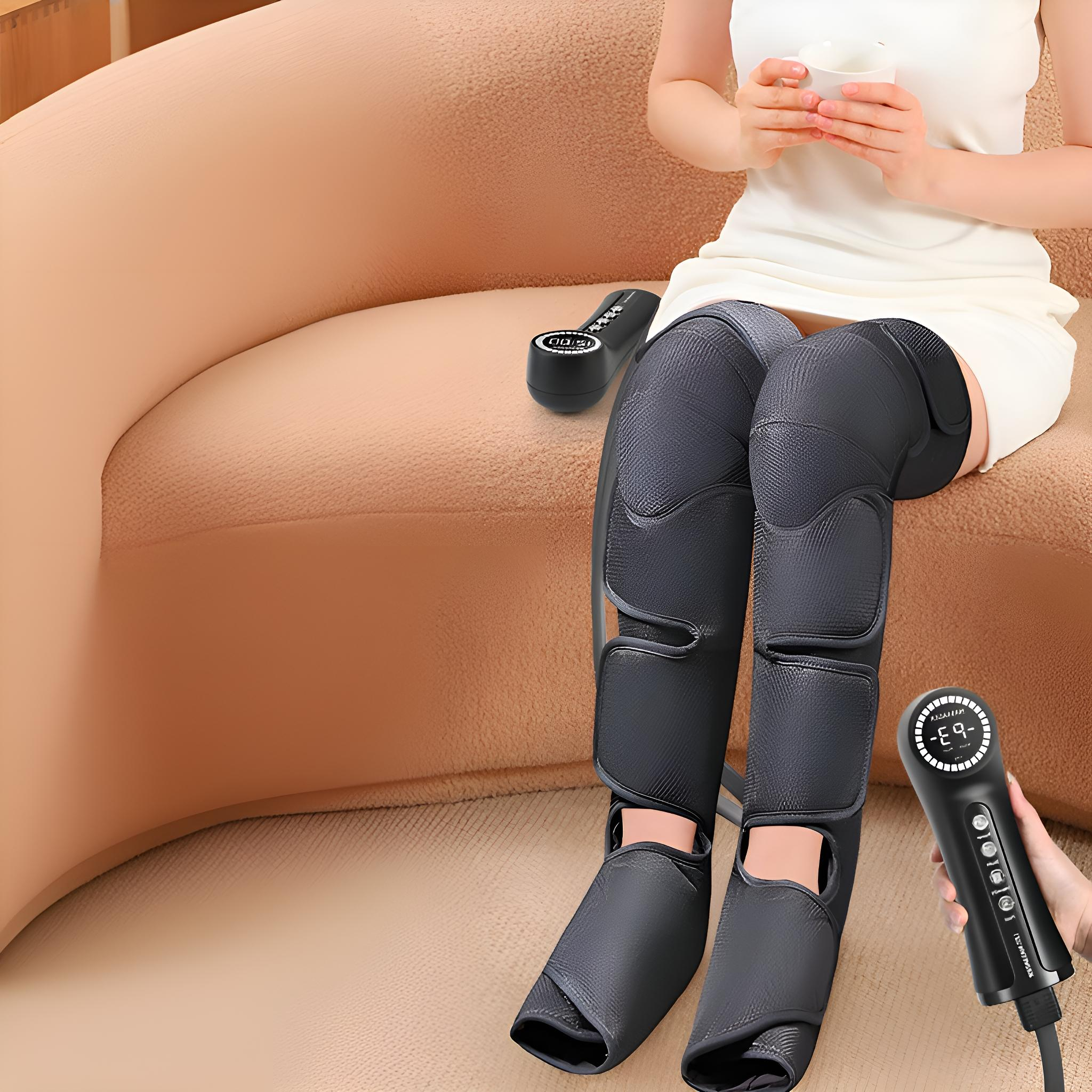 Eine Frau sitzt mit Beinmassagern und einem Controller auf einem beigen Sofa.