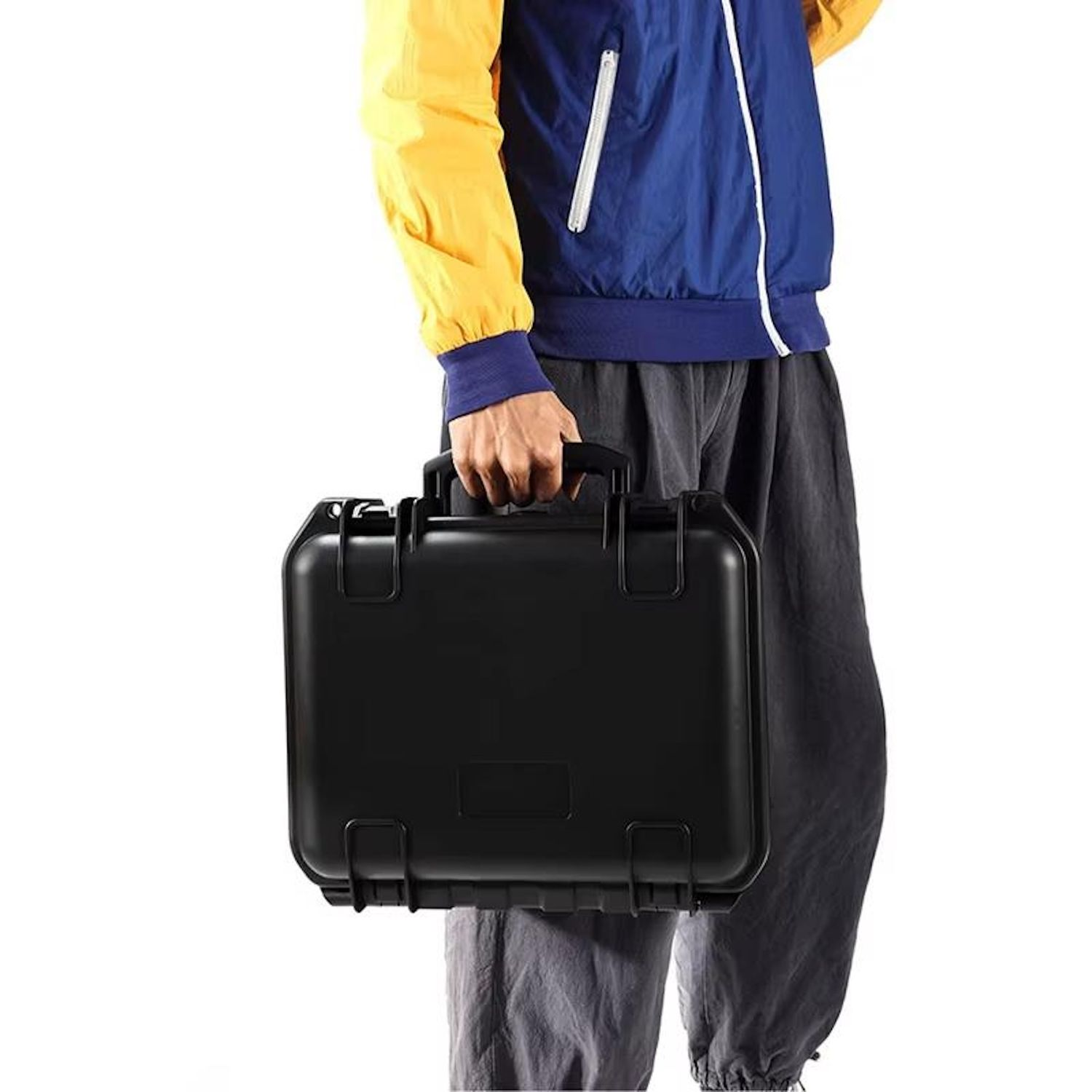 Person trägt einen schwarzen Hartschalenkoffer. Die Person trägt eine blaue Jacke und graue Hose.