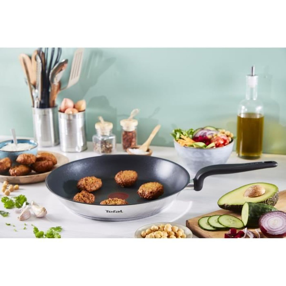Kochszene: Pfanne mit Essen, Gemüse, Ölflasche, Avocado und Salatschüssel auf weißer Oberfläche.