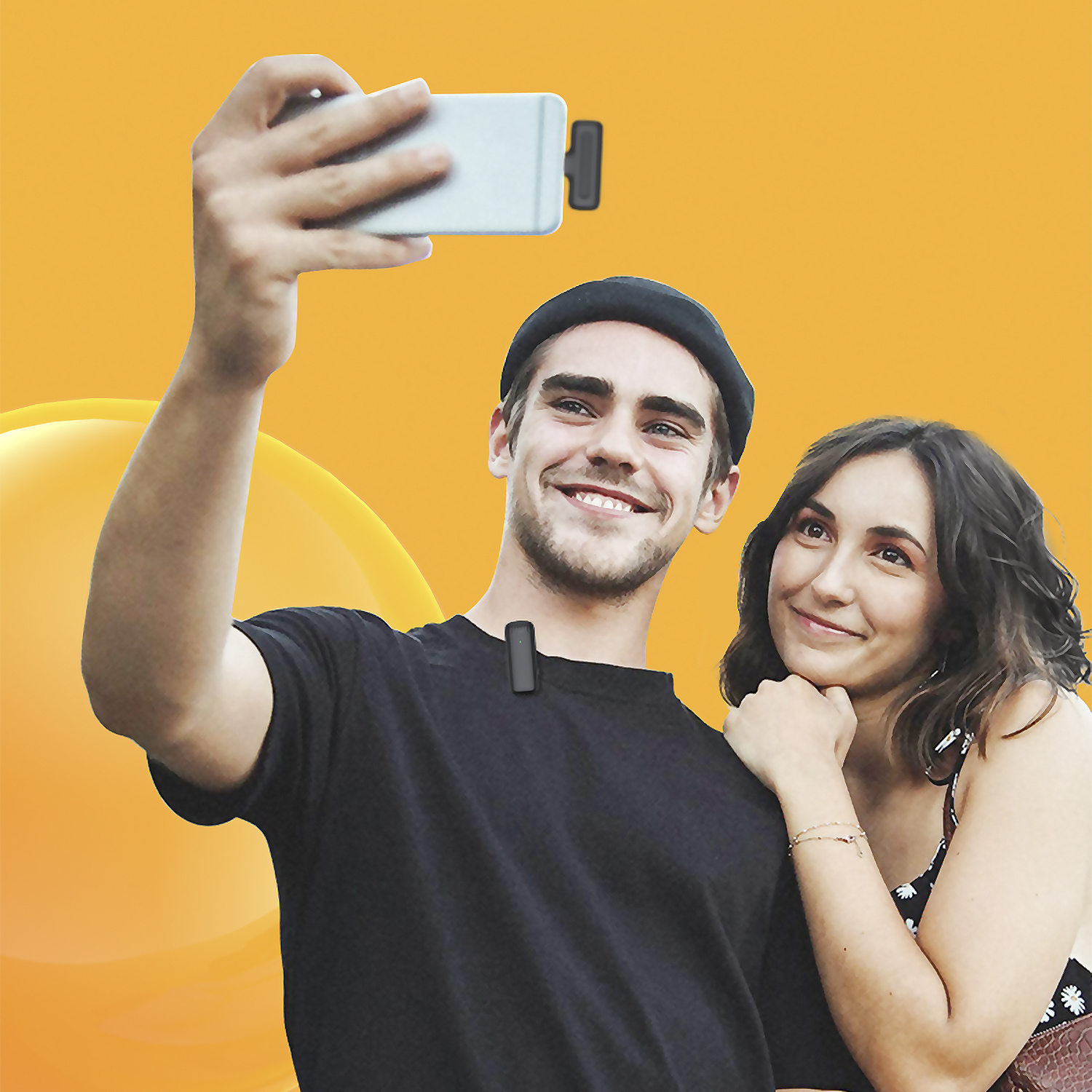 Hombre y mujer tomando selfie con teléfono y micrófono sobre fondo naranja.