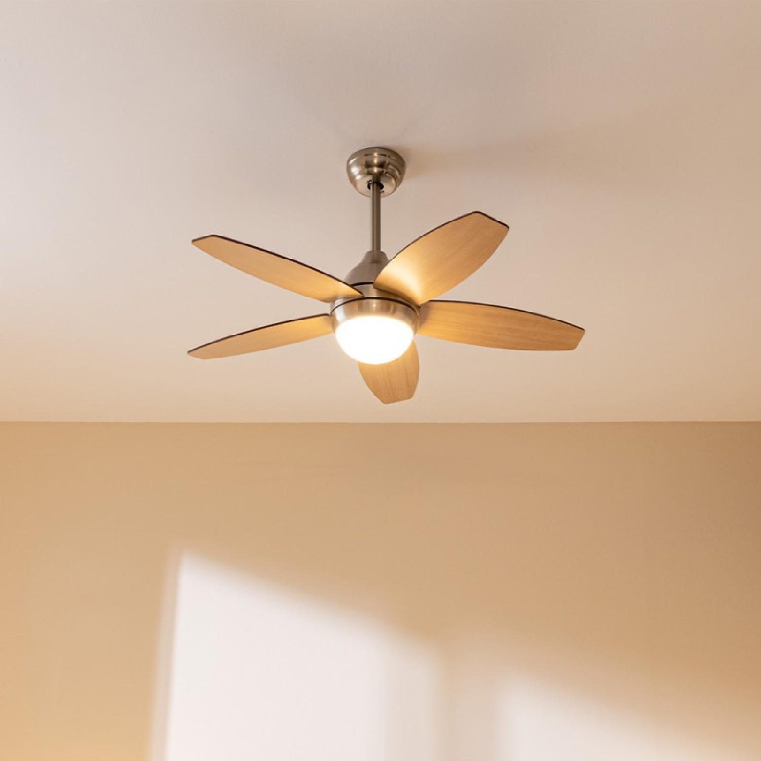 Un ventilatore da soffitto con cinque pale in legno chiaro, centro metallico e una lampada centrale.