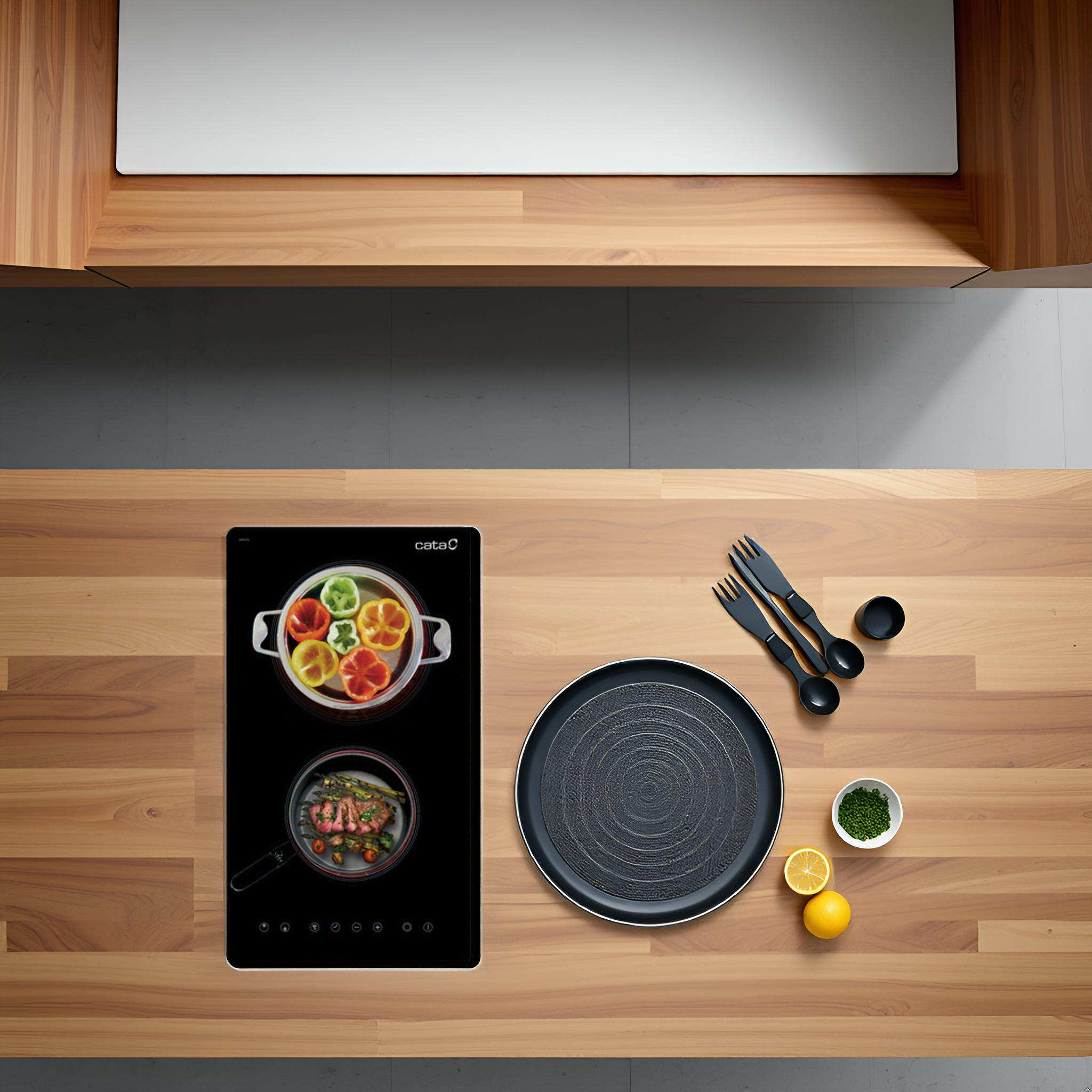 Vista cenital de una encimera de cocina con una placa de cocina negra, comida y utensilios. Fondo de madera.