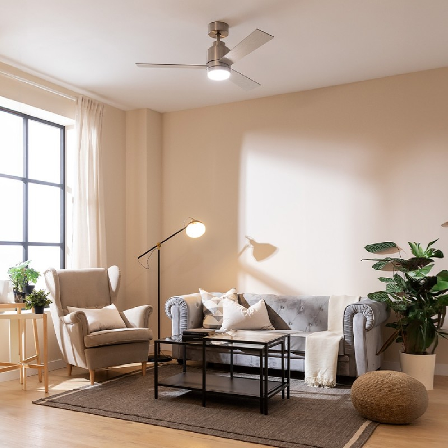 Salon z szarą sofą, fotelem i wentylatorem sufitowym. Duże okno i ciemny dywan.