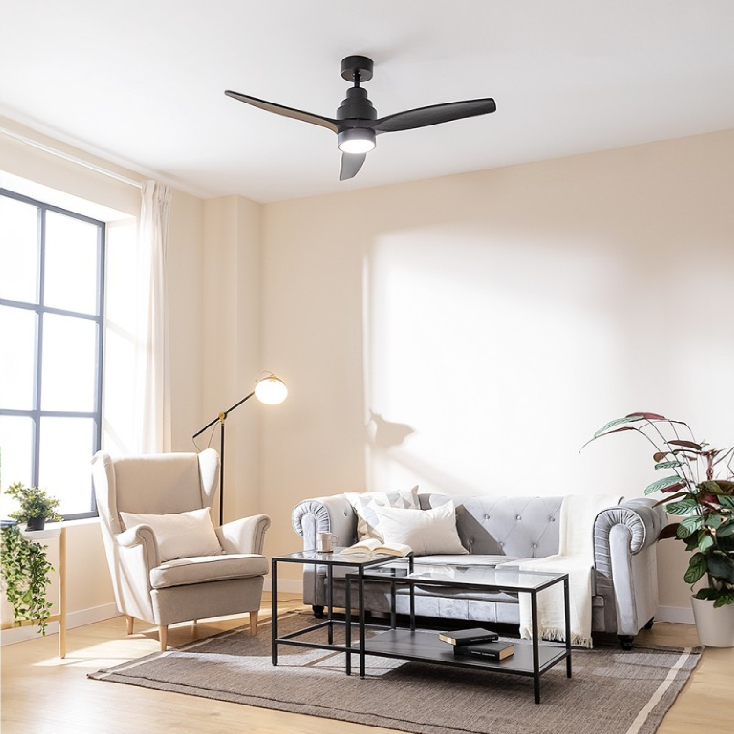 Salon z szarą sofą, fotelem, czarnym wentylatorem sufitowym i dużym oknem.