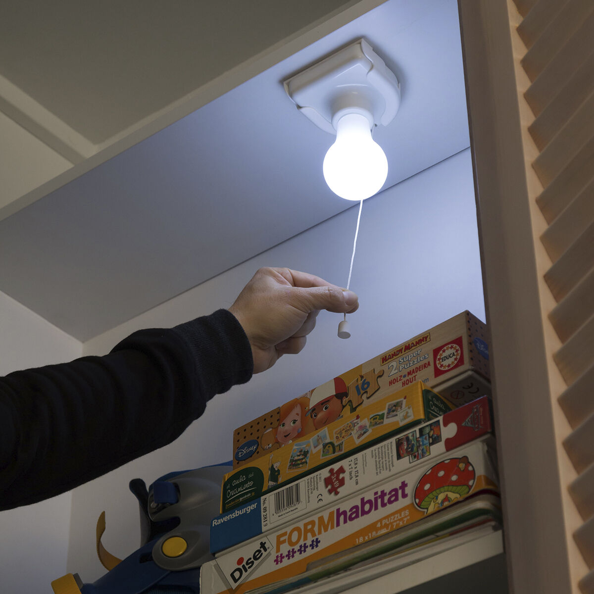 Una mano che tira una corda per accendere una lampadina attaccata al soffitto.