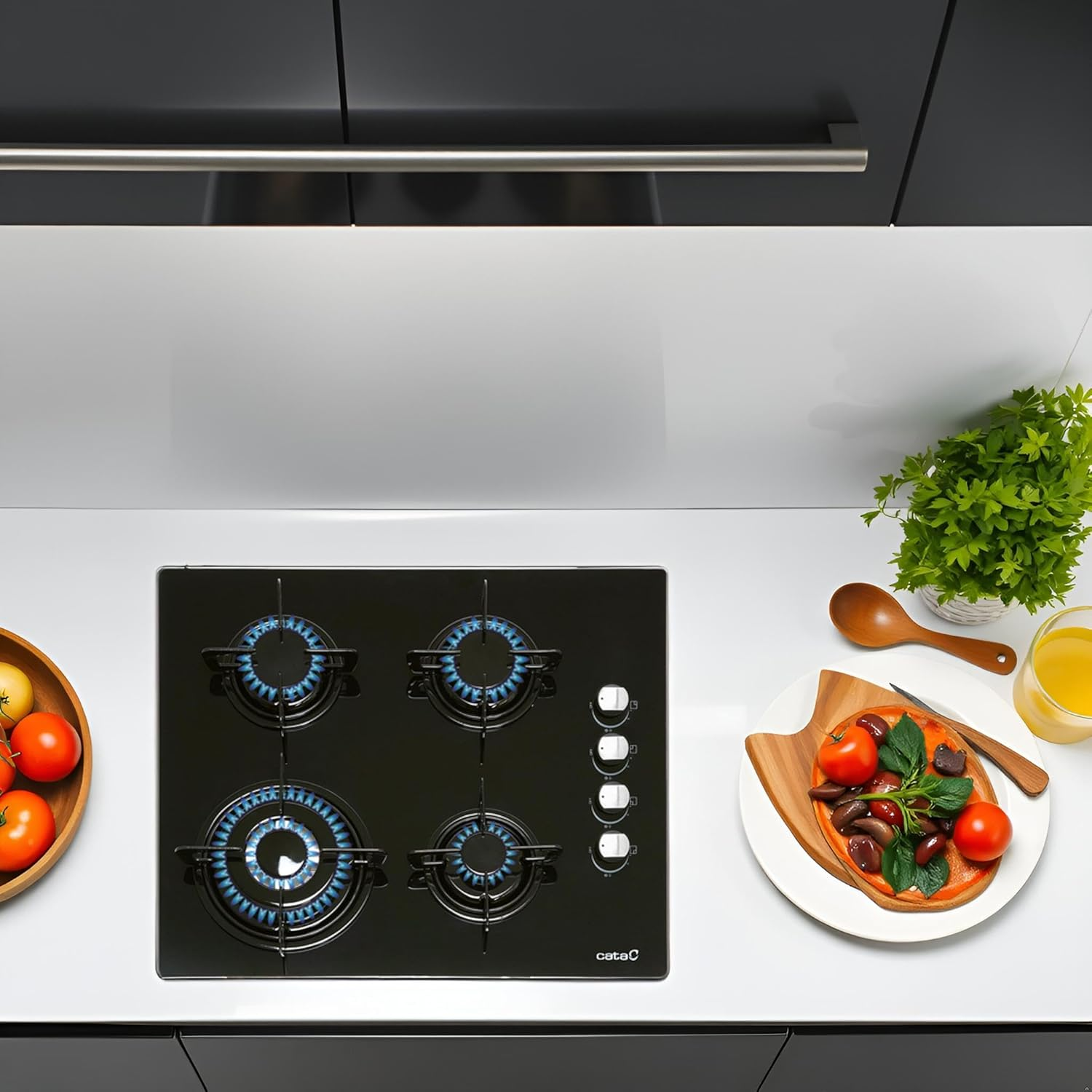 Czarna szklana płyta kuchenna z niebieskimi płomieniami, z przedmiotami kuchennymi wokół, widok z góry.