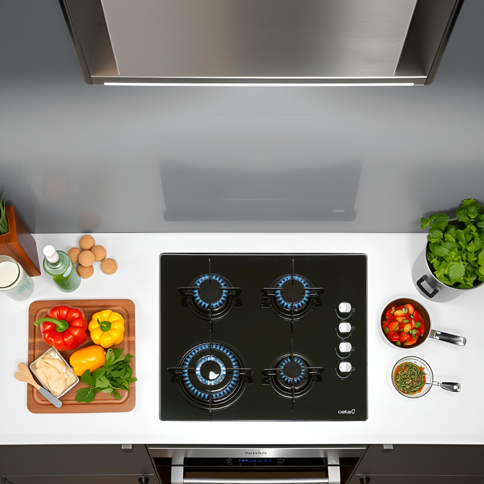 Widok z góry nowoczesnej kuchni z czarną kuchenką gazową, warzywami i przyborami kuchennymi na białym blacie.