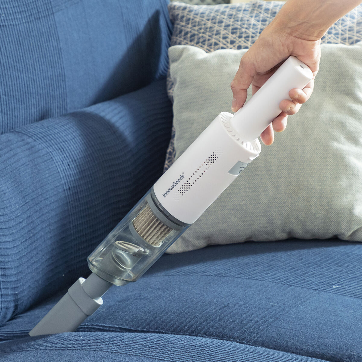 Mano che tiene un aspirapolvere portatile bianco, che pulisce un divano blu.