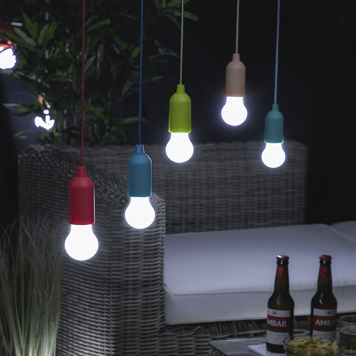 Escena al aire libre con luces de colores colgantes y botellas de cerveza en una mesa.