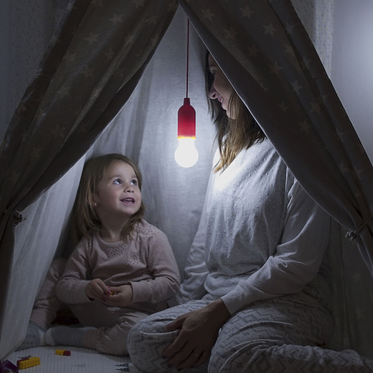 Madre e hija en una tienda de campaña, iluminadas por una bombilla roja colgante.