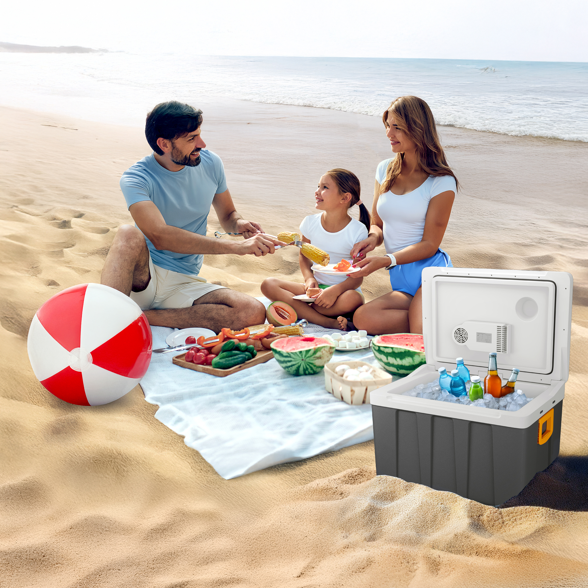 Familienpicknick am Strand mit Kühler, Essen, Strandball und Meer im Hintergrund.