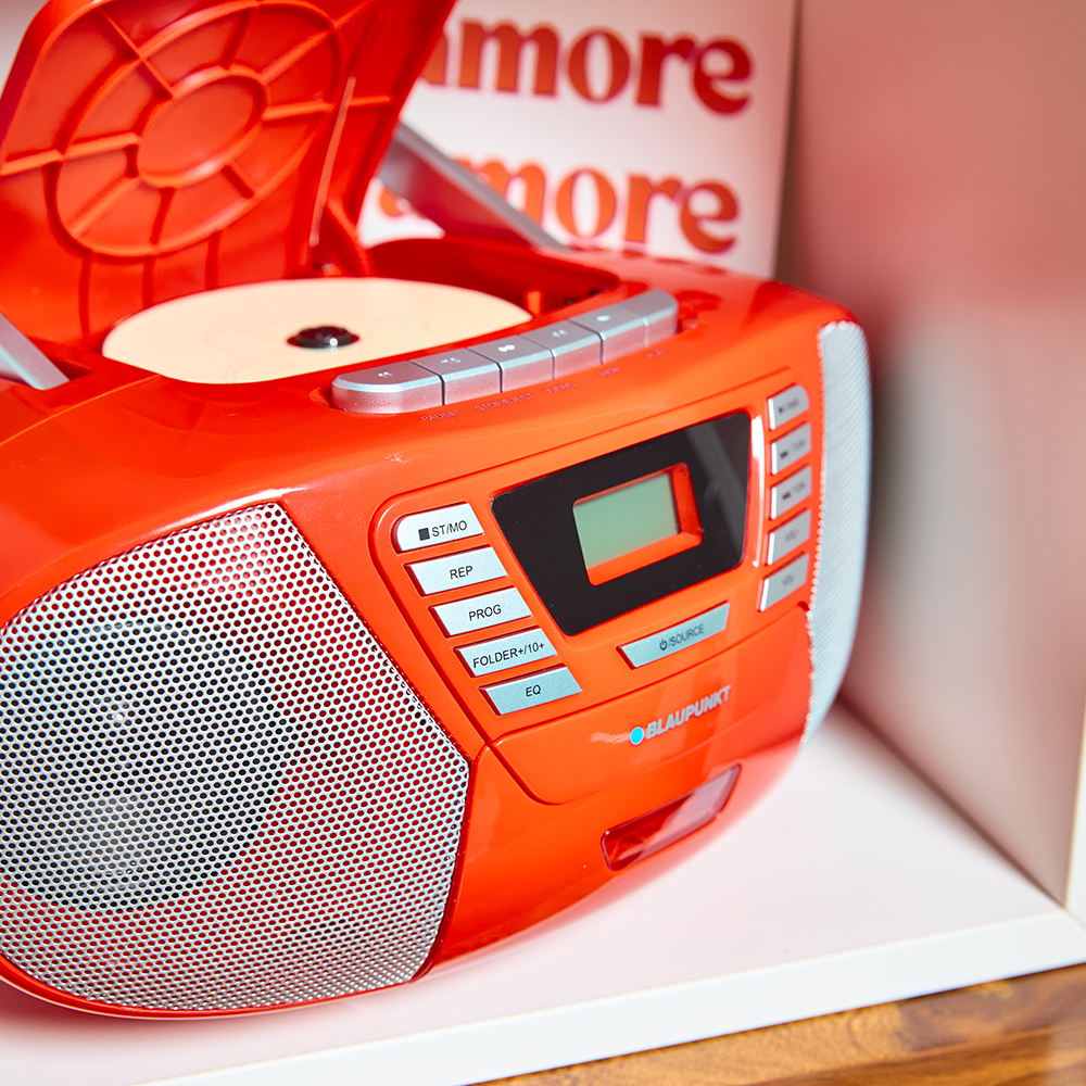 Orangene Boombox mit offenem CD-Player, Knöpfen und Display. Weißes Regal, Hintergrund.