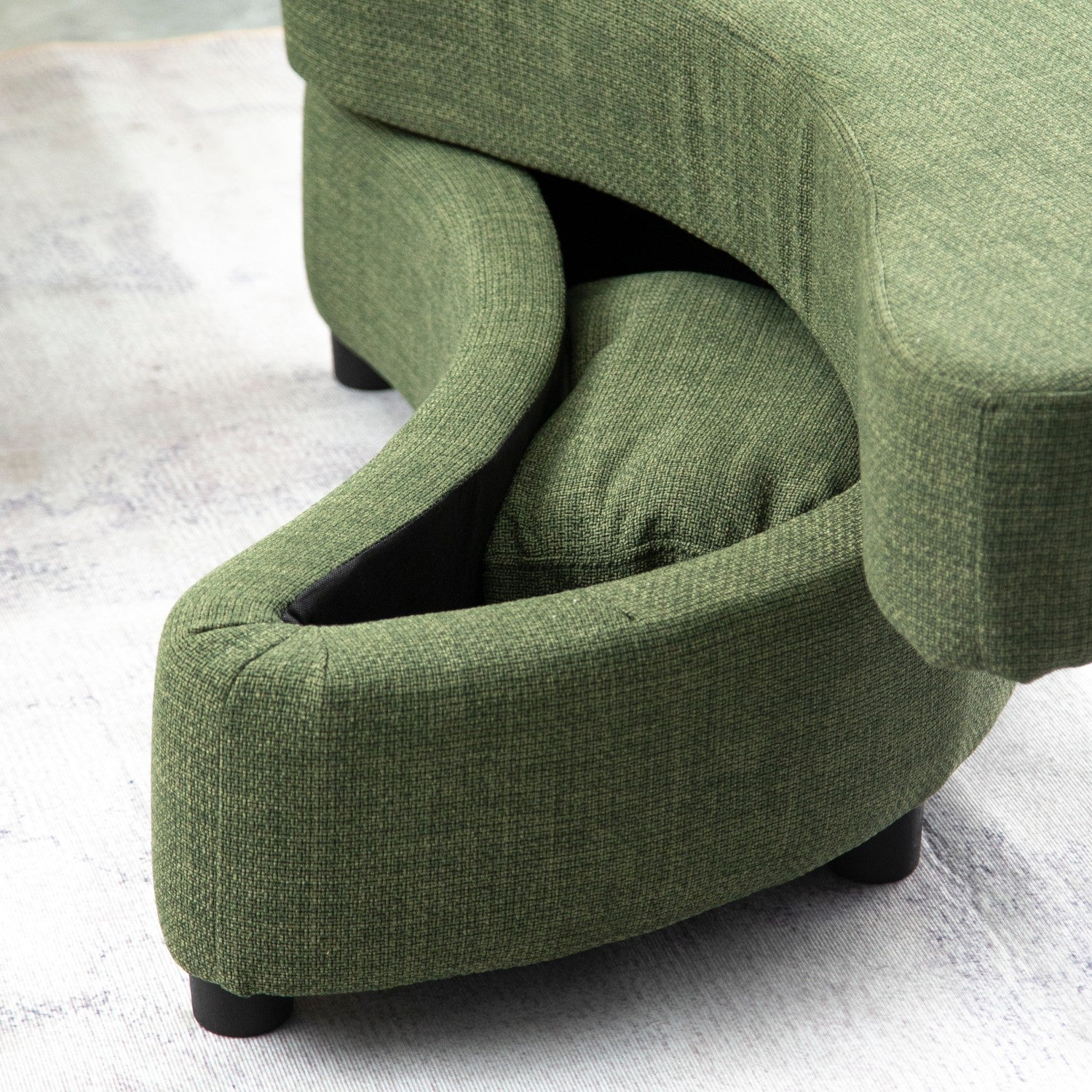 Ein grünes, gebogenes Sofa mit einem versteckten Fach, auf einem gemusterten Teppich.