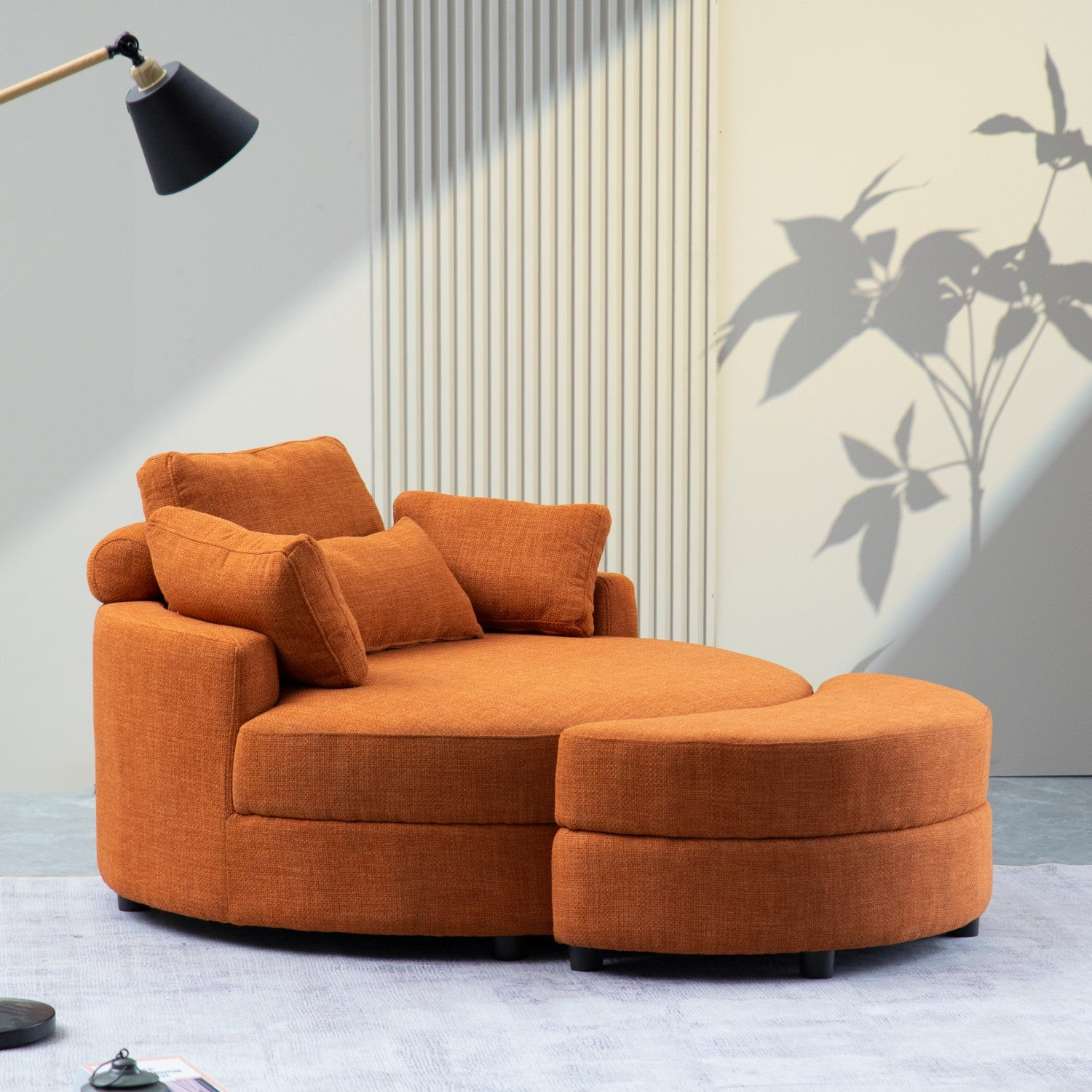 Sofá naranja con un reposapiés. La habitación está iluminada con luz natural y una lámpara. Sombra de una planta en la pared.