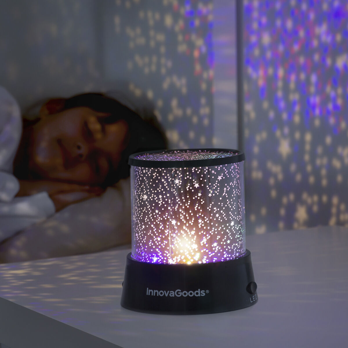 Lampada proiettore di stelle con stelle proiettate sulla parete e sul soffitto. Una persona dorme vicino.
