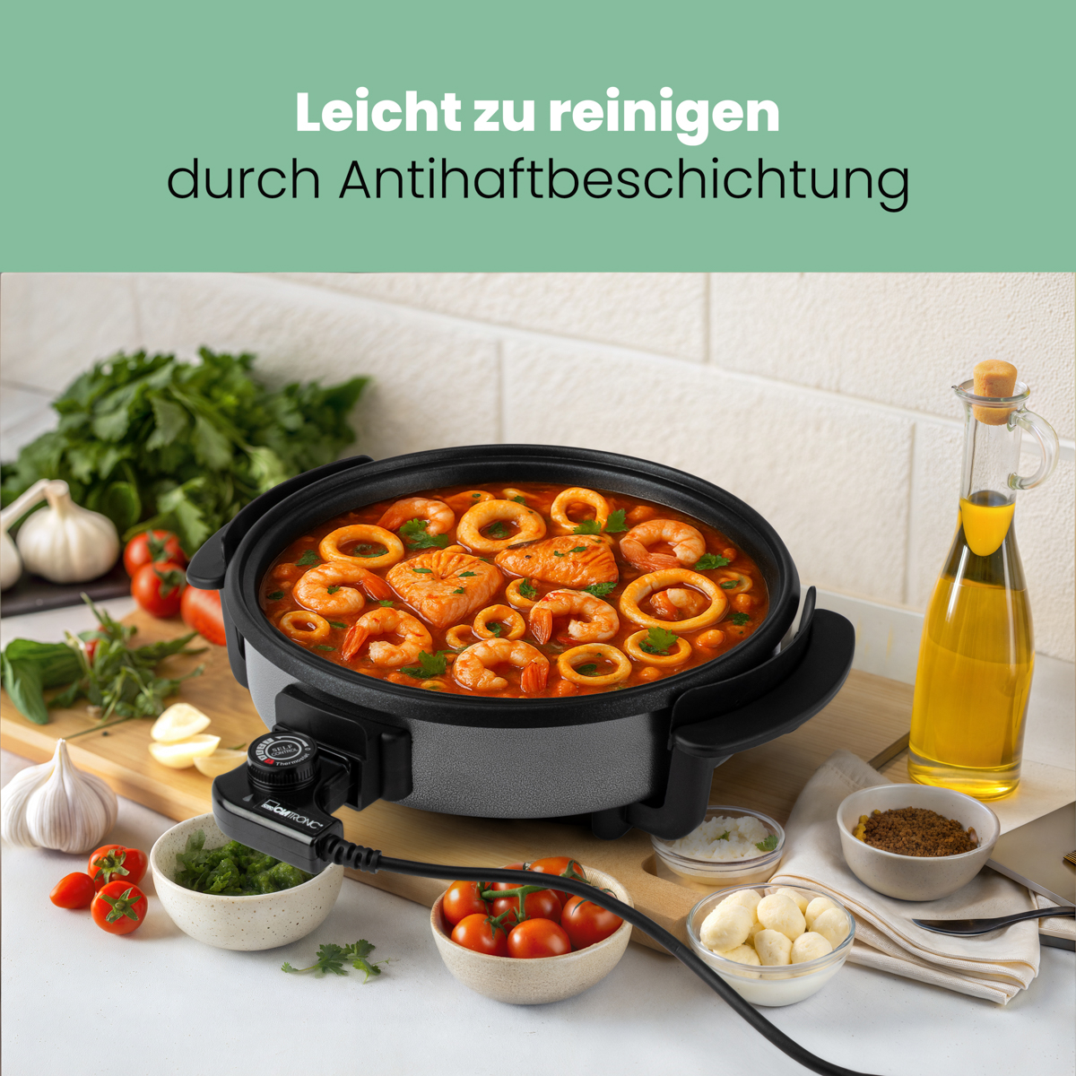 Patelnia elektryczna z jedzeniem w środku. Tekst: Łatwe czyszczenie dzięki powłoce nieprzywierającej. Jedzenie to owoce morza.