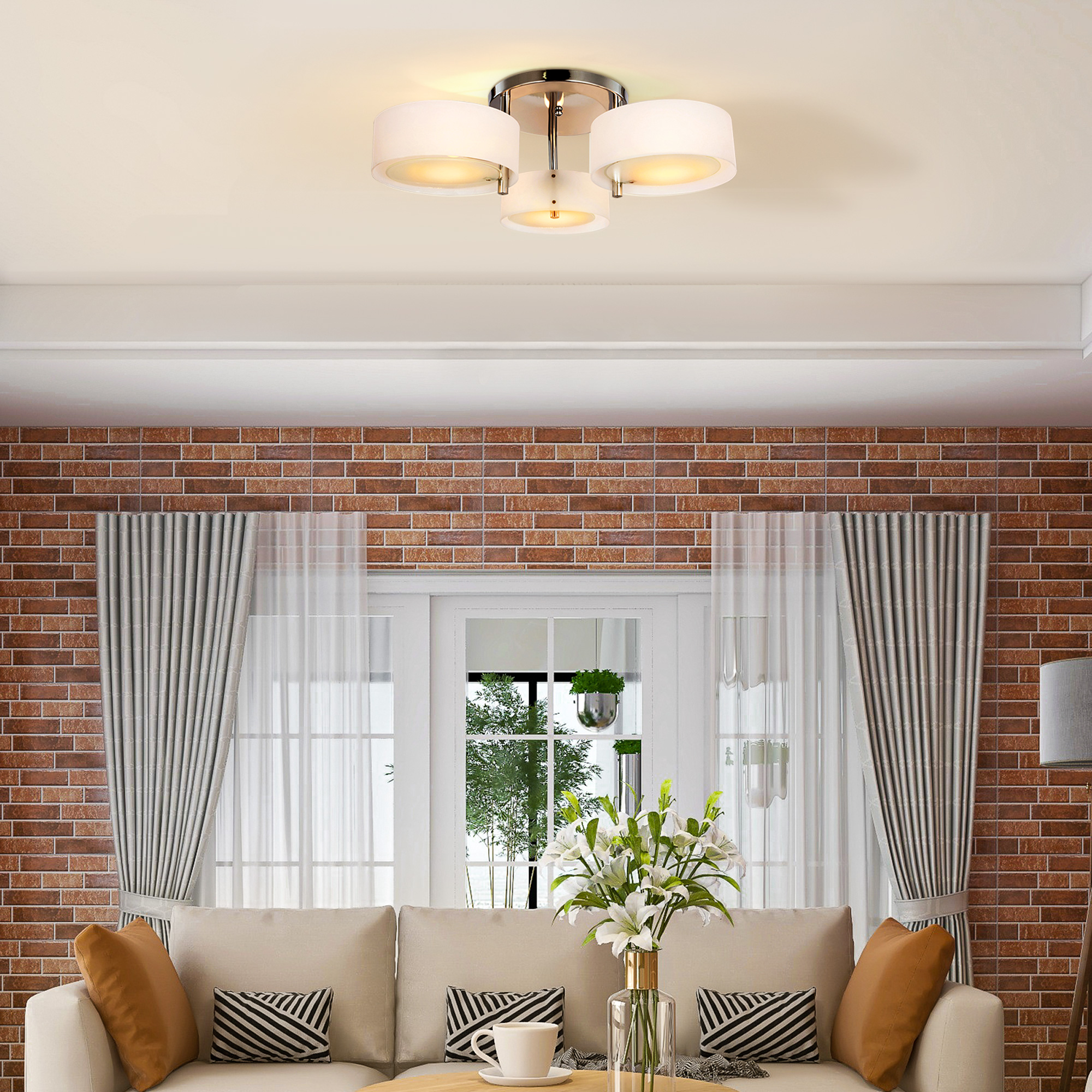 Una lámpara de techo con tres luces. Está montada en un techo blanco sobre una habitación con una pared de ladrillo.