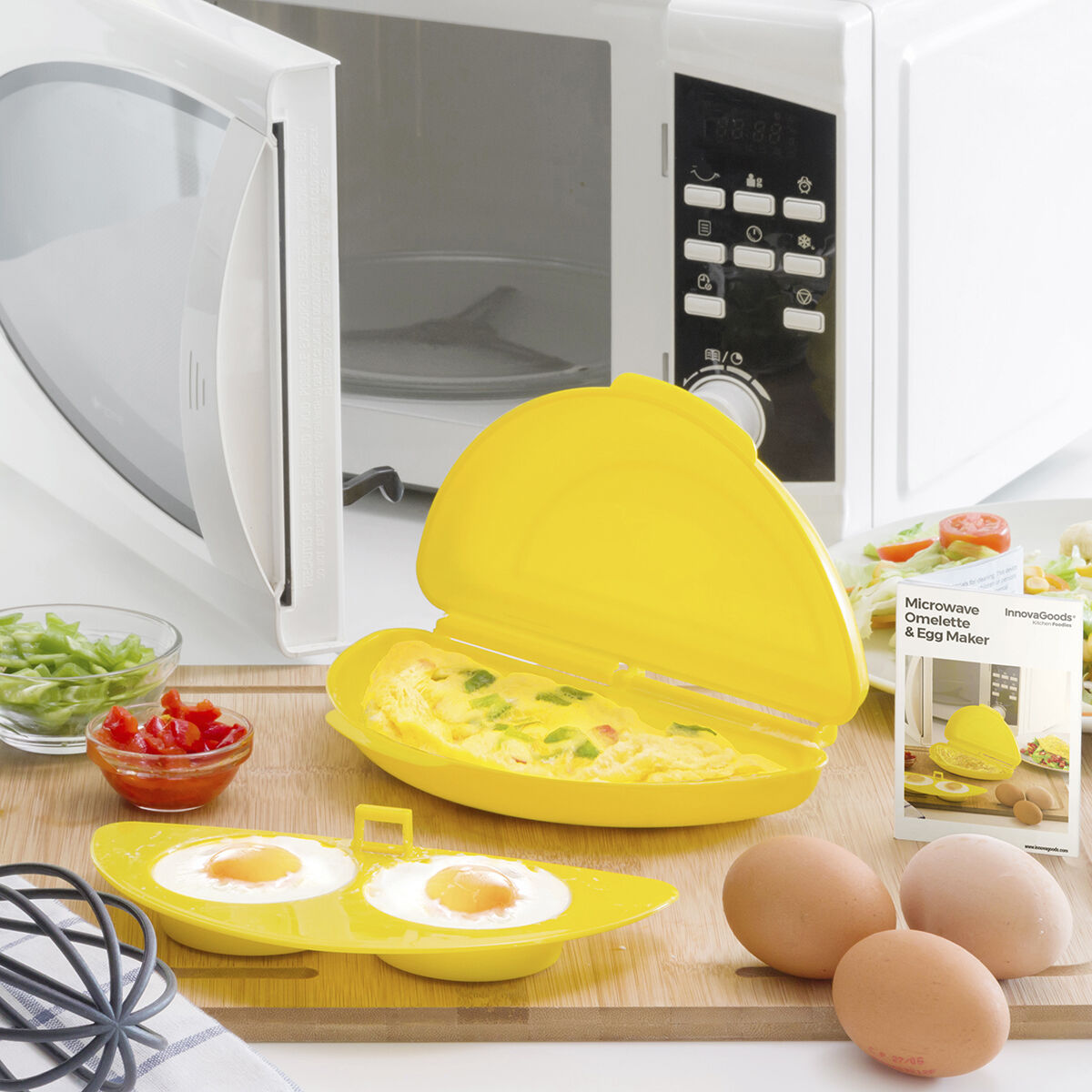 Omeletiera y huevos sobre una tabla de madera. Al lado hay verduras y un microondas.