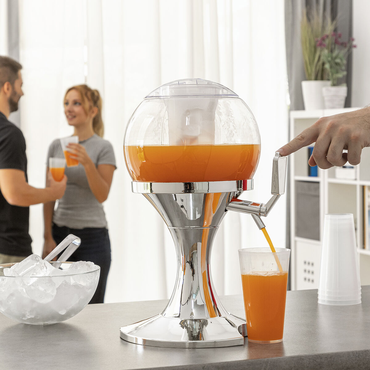 Getränkespender mit orangefarbener Flüssigkeit, Eisschale und Personen im Hintergrund.