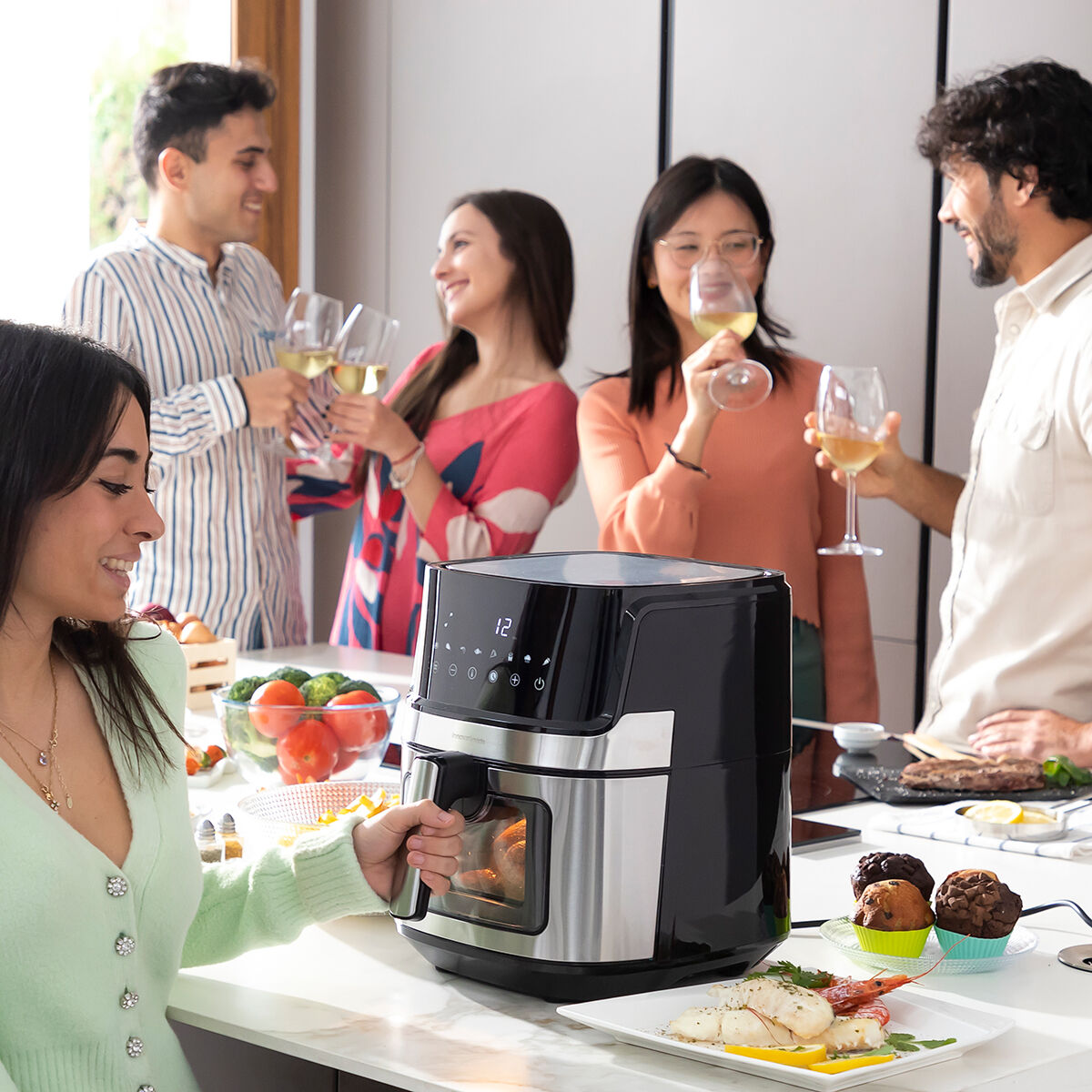 Persone brindano con vino vicino a una friggitrice ad aria con cibo.