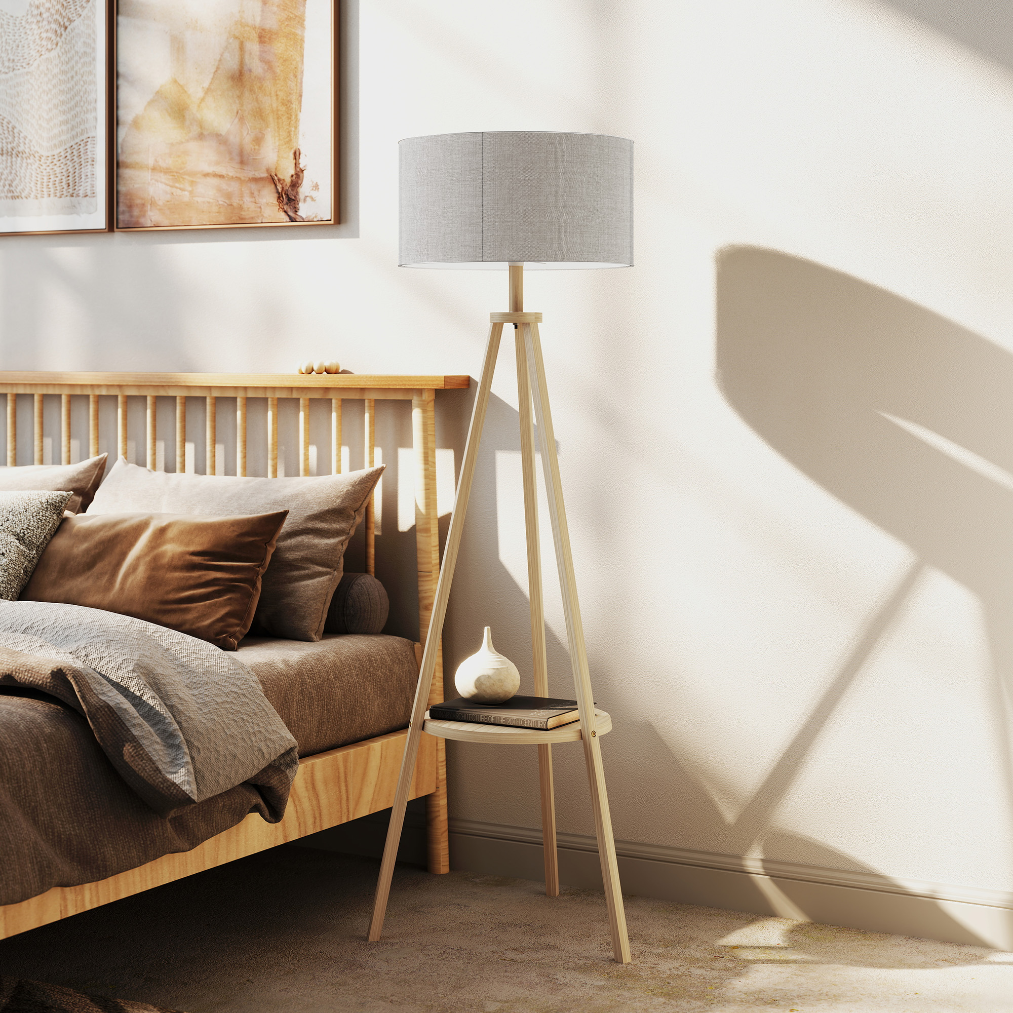Lámpara de pie trípode de madera con pantalla gris, sobre una mesa pequeña, cerca de una cama.