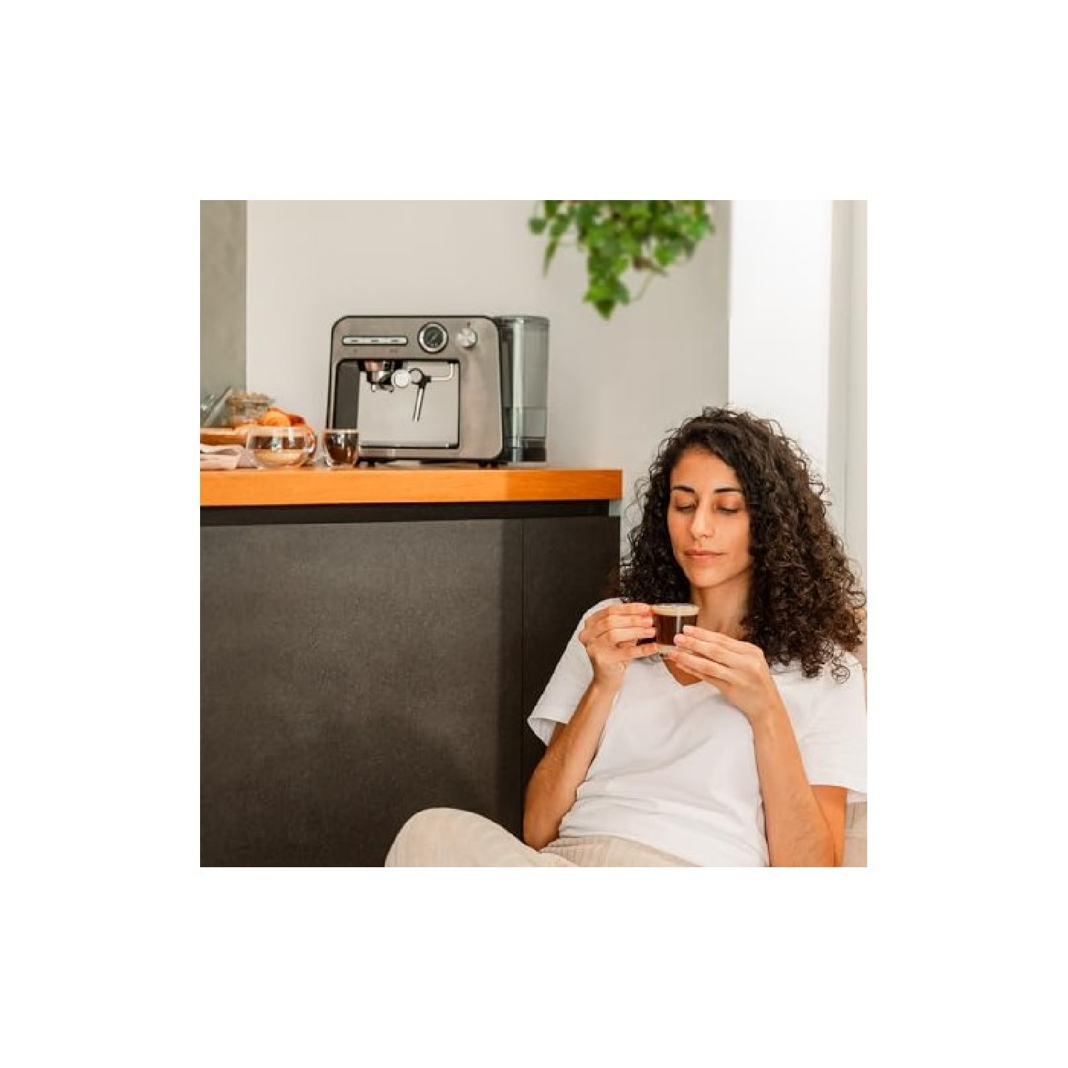 Kobieta pije kawę z filiżanki obok ekspresu do kawy na blacie.