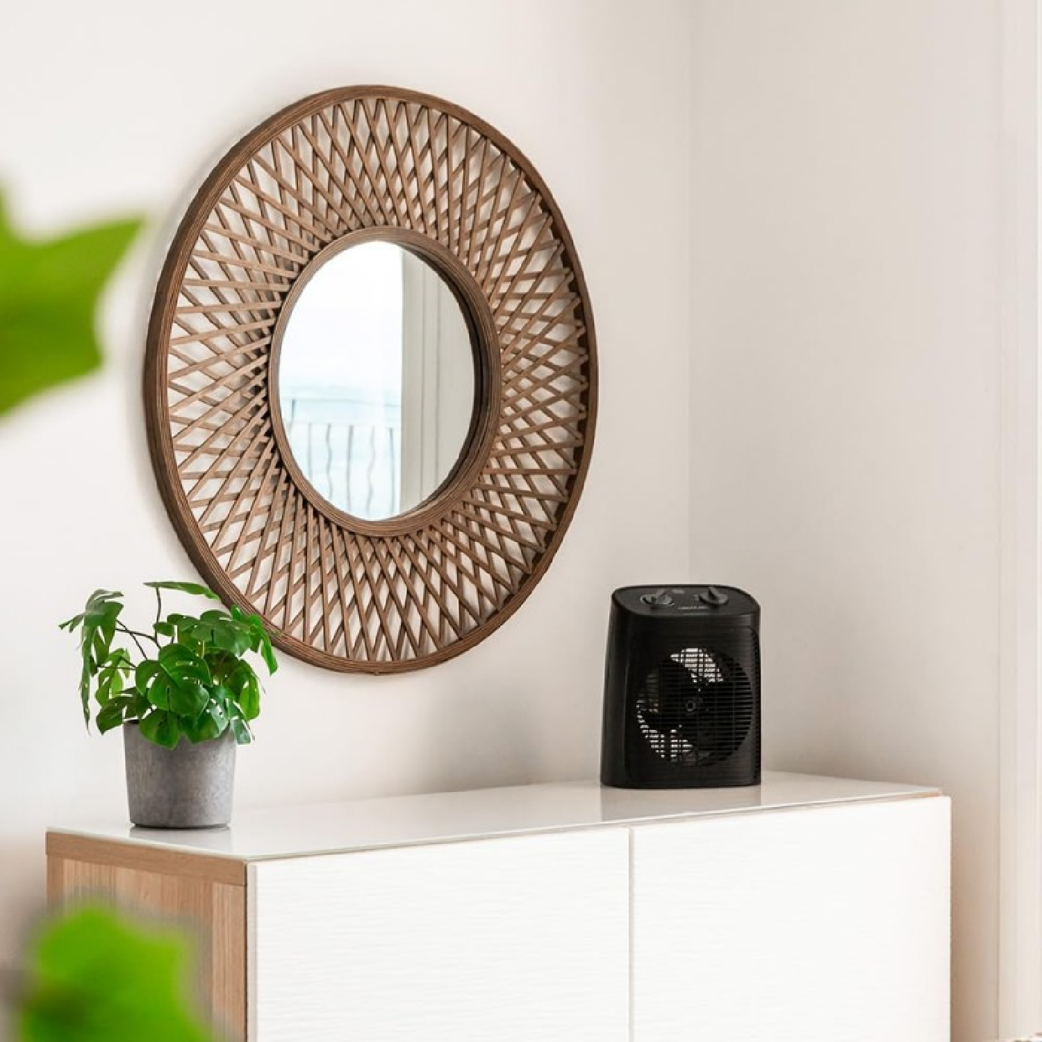 Pokój z białą szafką, okrągłym lustrem i rośliną. Czarny grzejnik na szafce.
