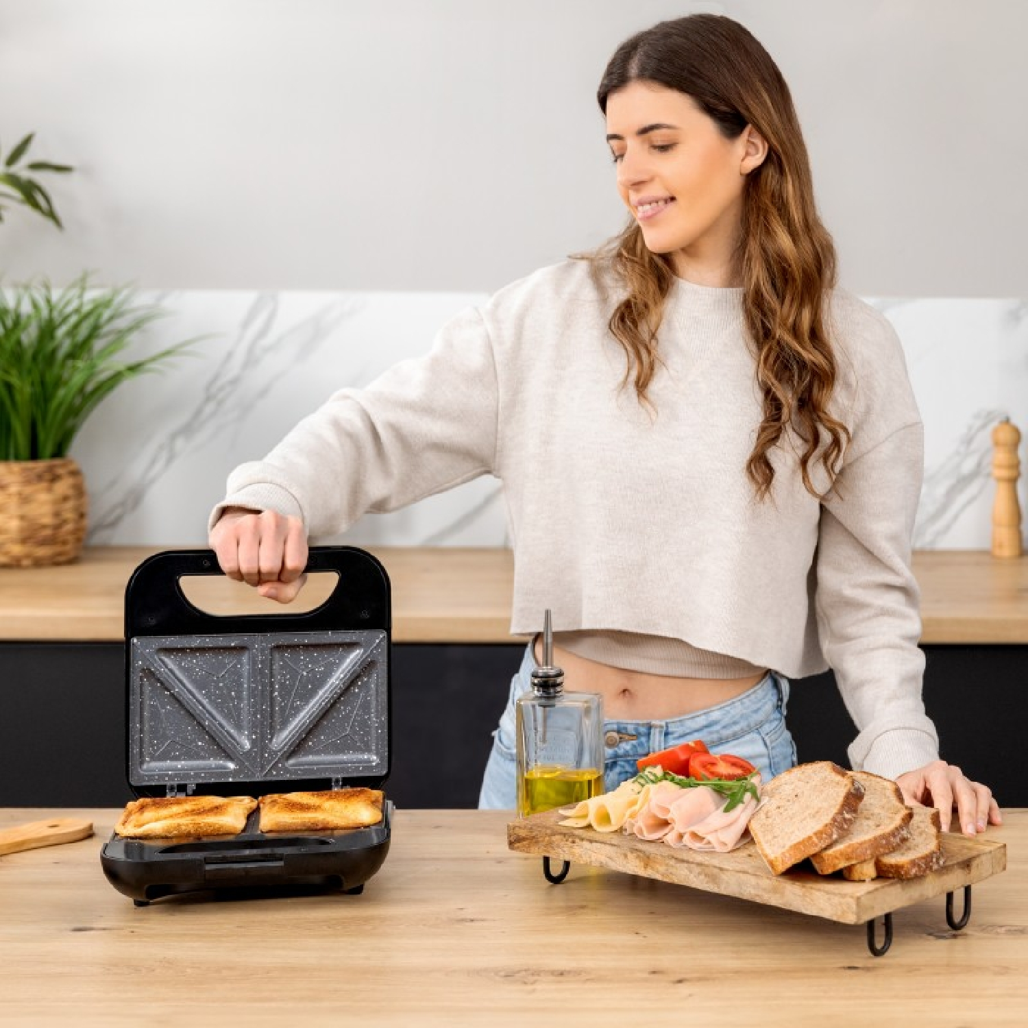 Una donna fa un panino con una sandwich maker. Cibo e ingredienti visibili.
