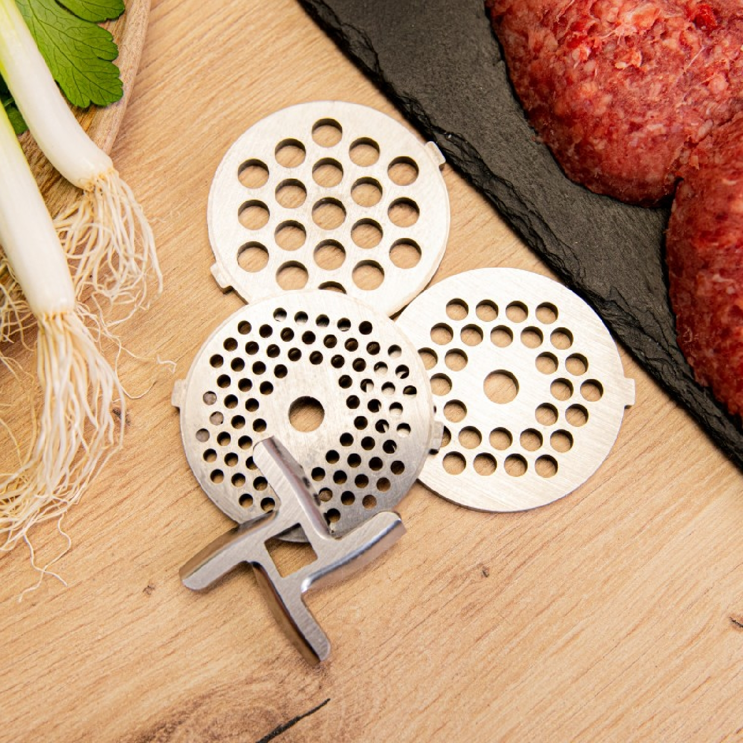 Parti di tritacarne. 3 piastre metalliche rotonde forate e una vite. Sfondo in legno.
