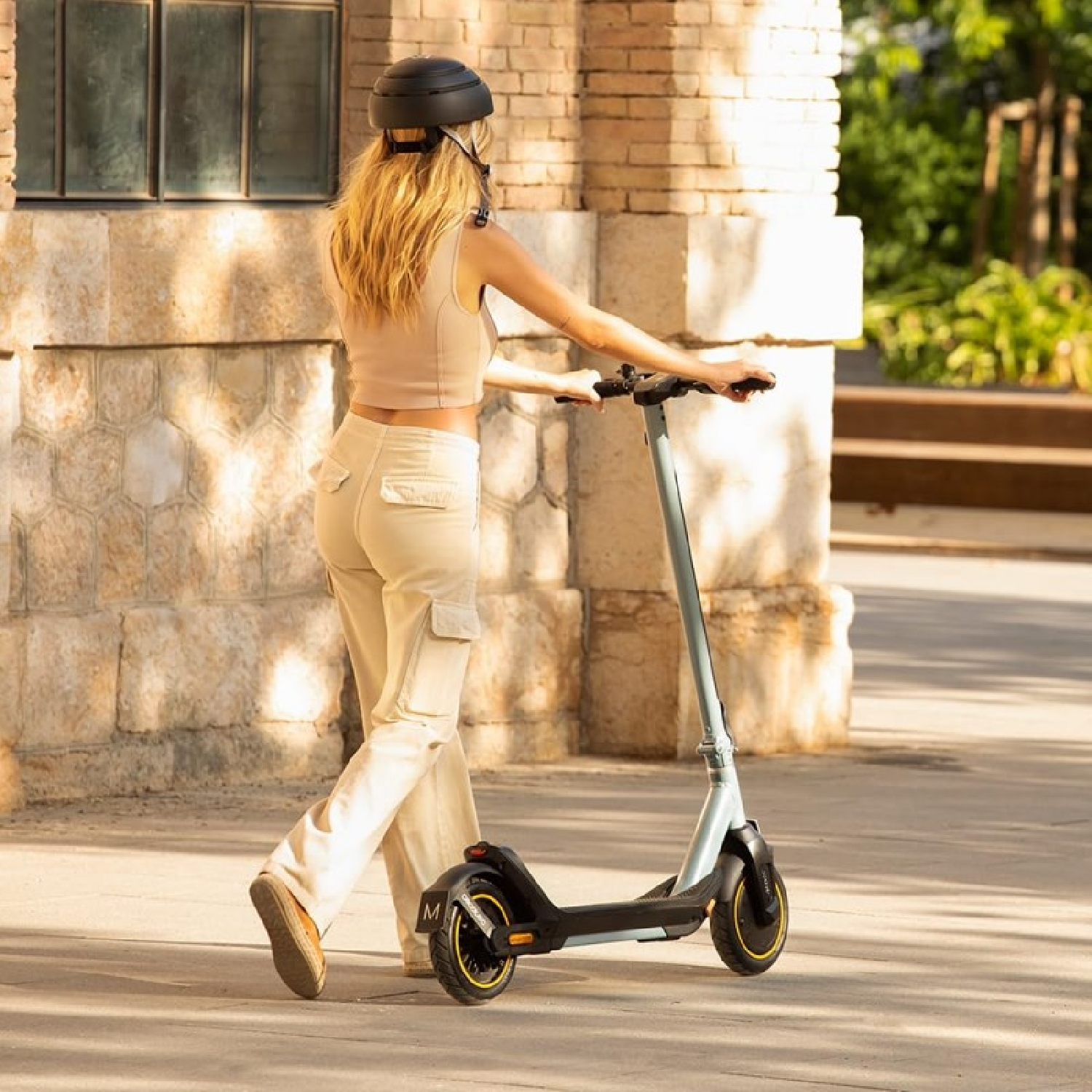 Kobieta na skuterze, w kasku. Tło: ceglana ściana.