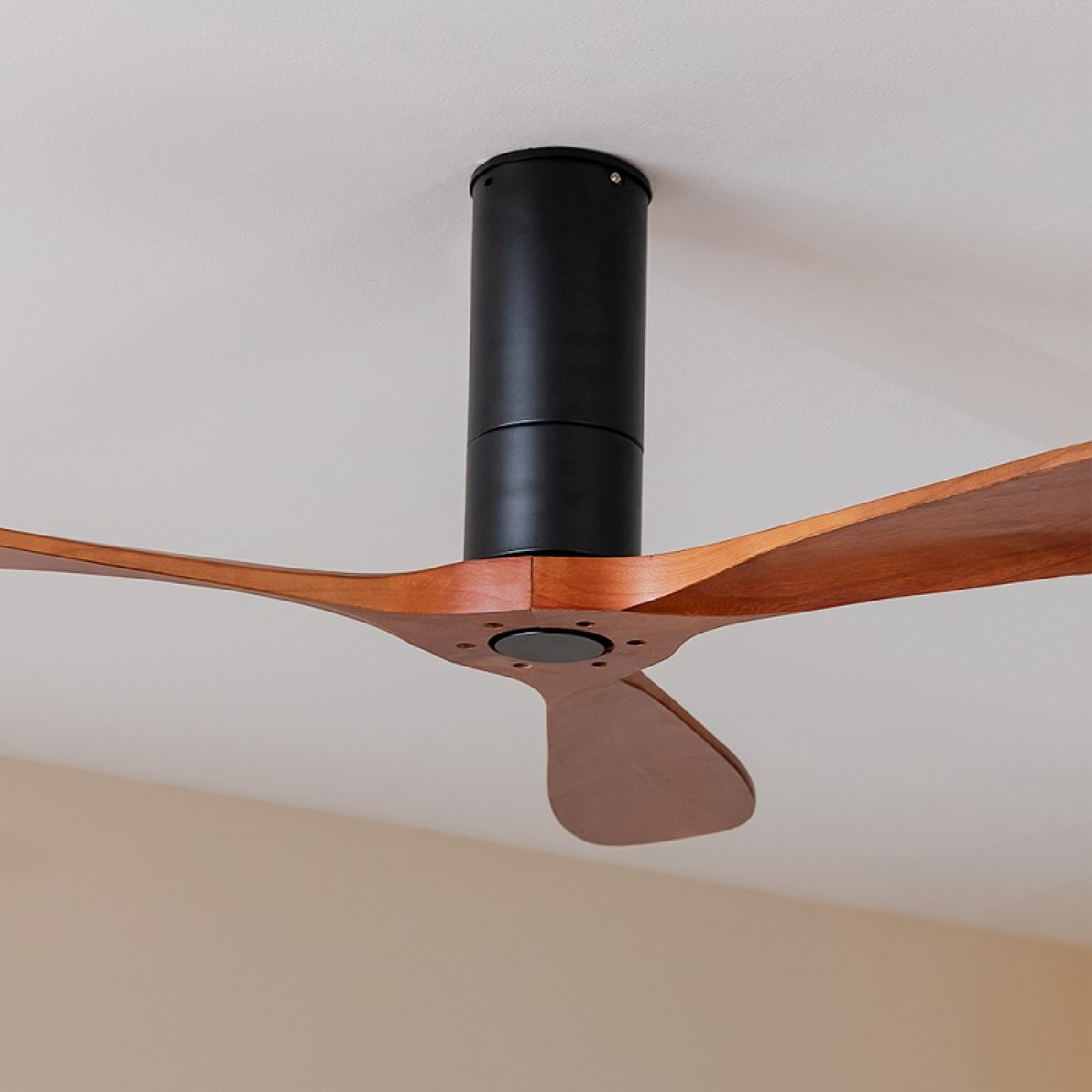 Wentylator sufitowy z drewnianymi łopatami i czarnym silnikiem. Biały sufit.